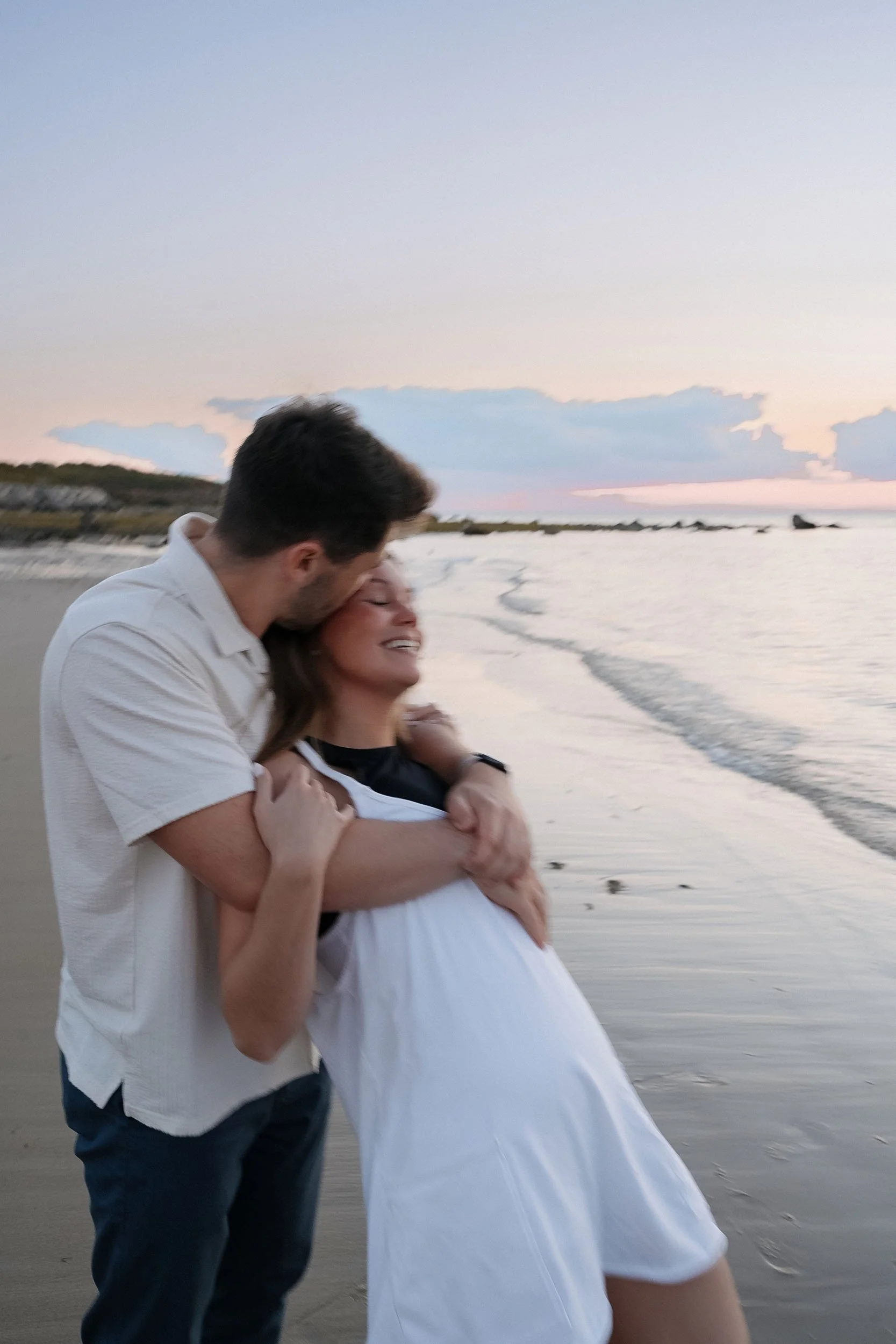 A couple embracing and kissing on a beach at sunset.