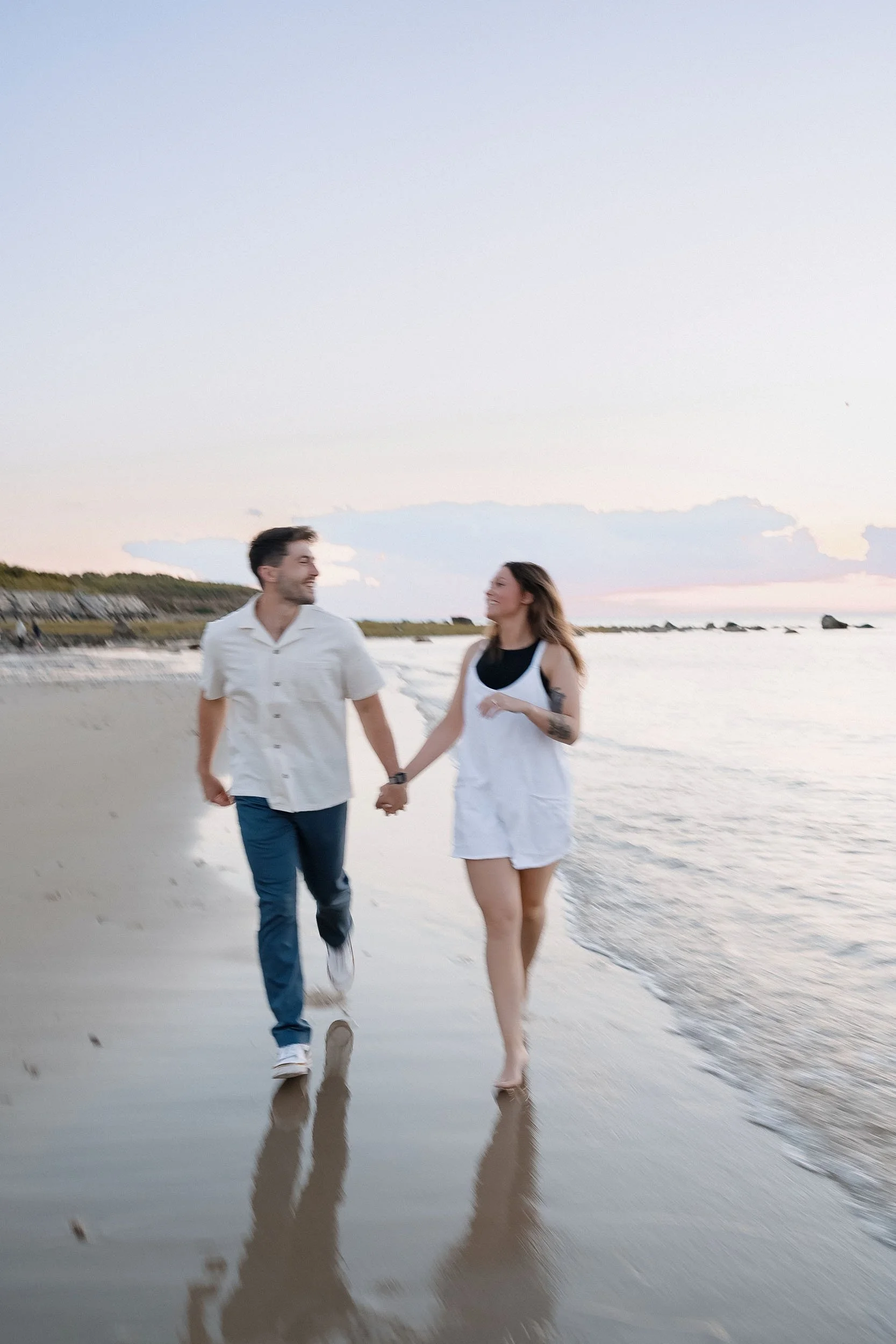 A couple holding hands and walking barefoot on the beach at sunset, smiling and enjoying each other's company.