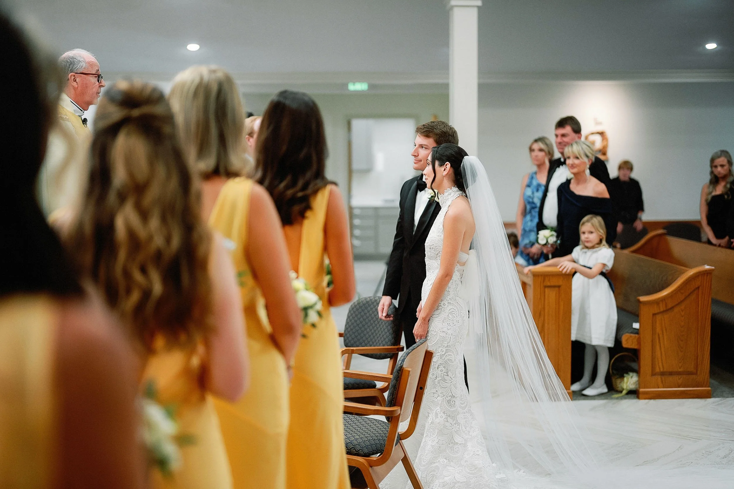 A wedding ceremony with the bride and groom standing before a minister, surrounded by friends and family in a church or chapel.