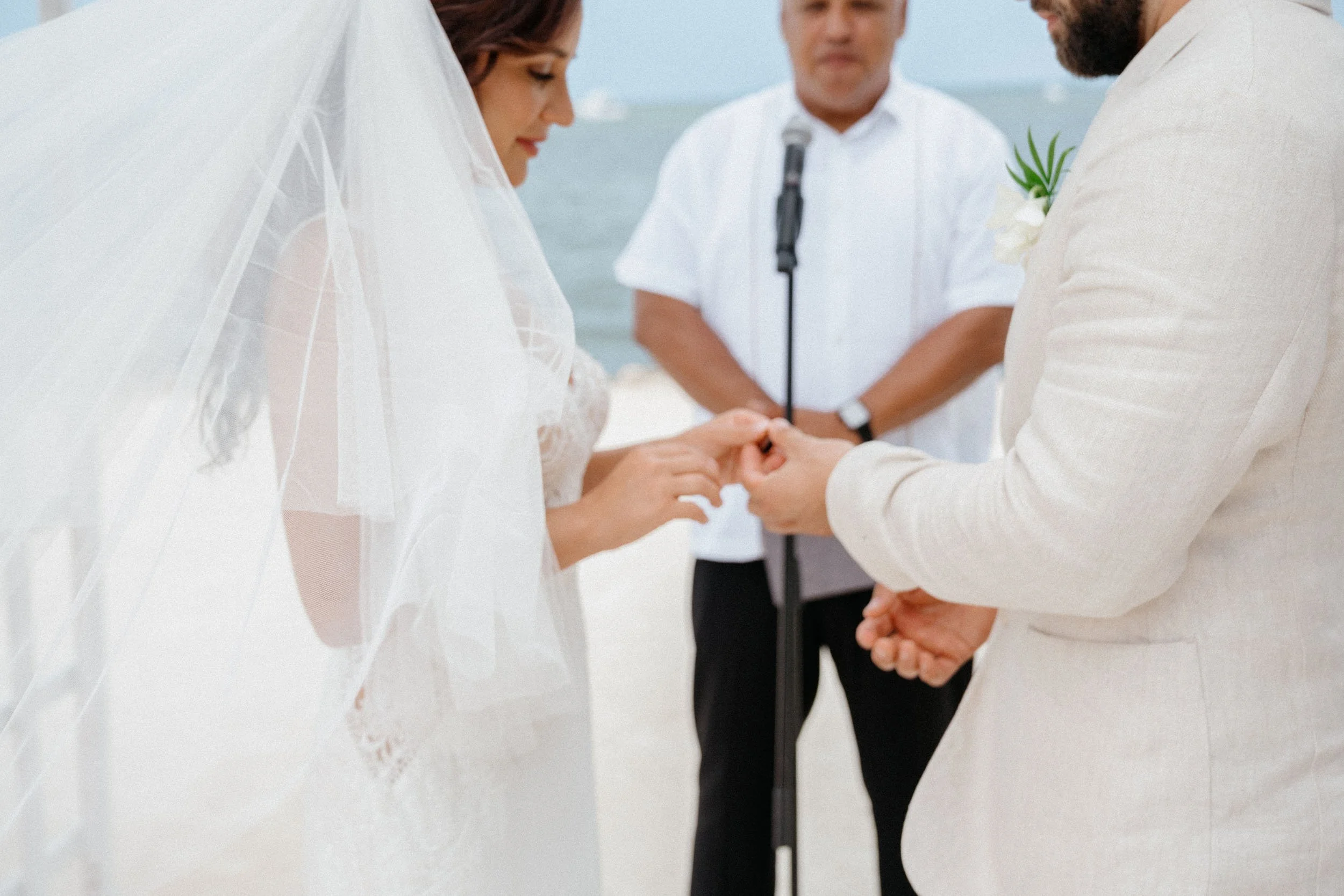Bride and groom exchanging rings during their beach wedding ceremony with officiant in the background.