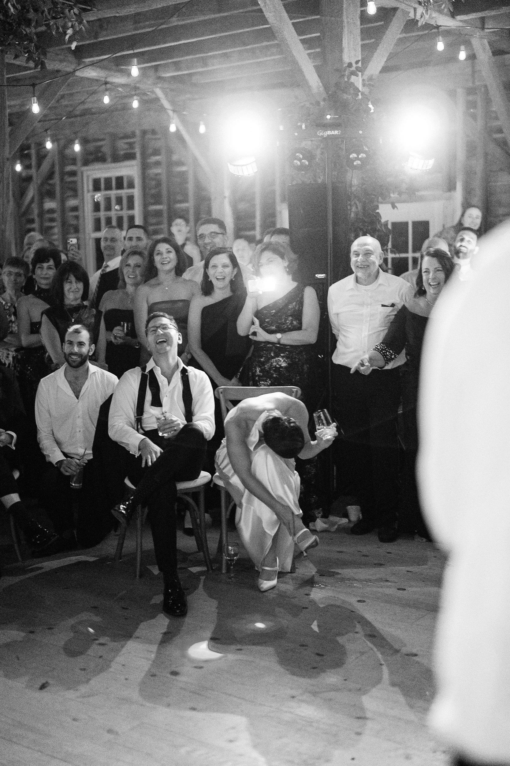 A group of people at a wedding reception, enjoying and laughing, with a dancing bride and groom in the foreground.