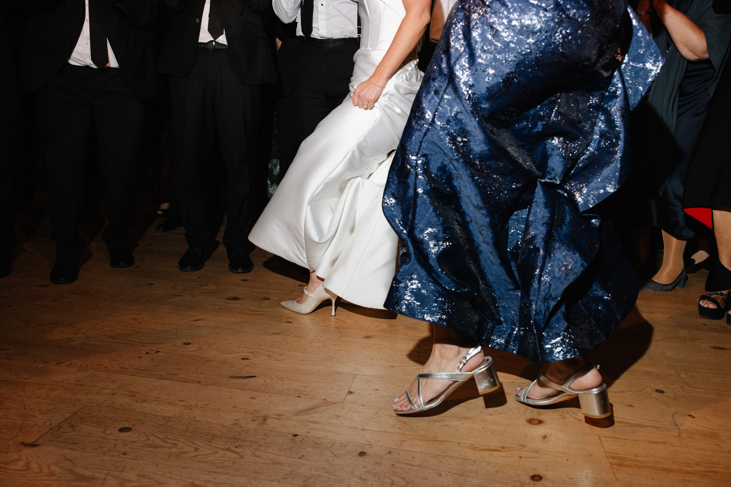 Guests dancing at a wedding reception, featuring women in fashionable dresses and heels, with a wooden dance floor.