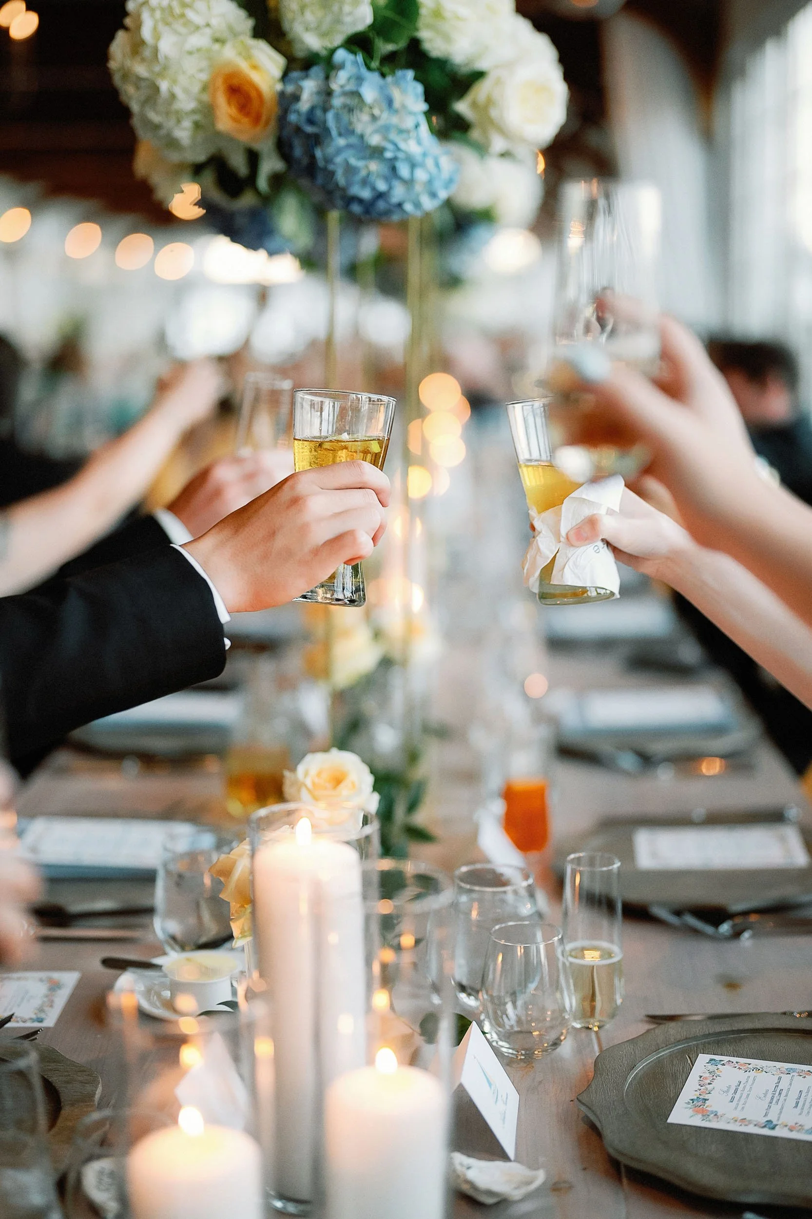 People are raising glasses of champagne or sparkling wine at a decorated wedding reception table, with candles and floral centerpieces.