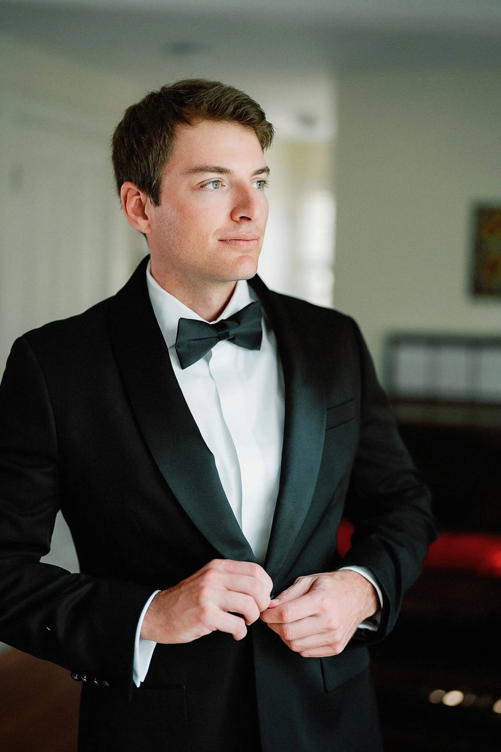 Young man in a black tuxedo and bow tie adjusting his suit.