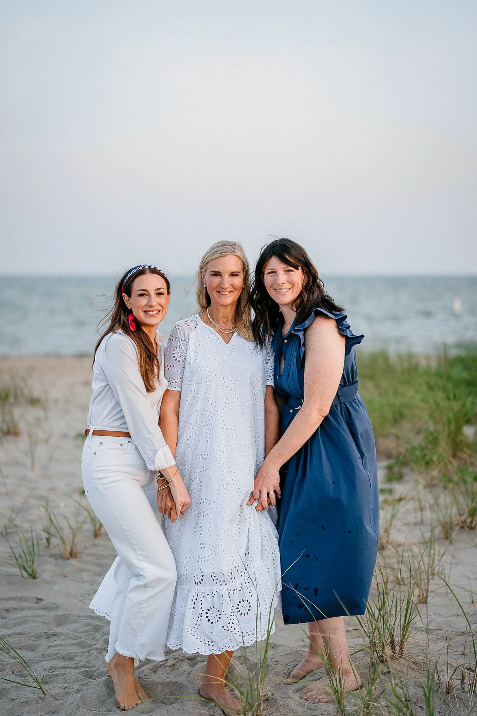 Three women standing on the beach near the ocean, smiling at the camera.