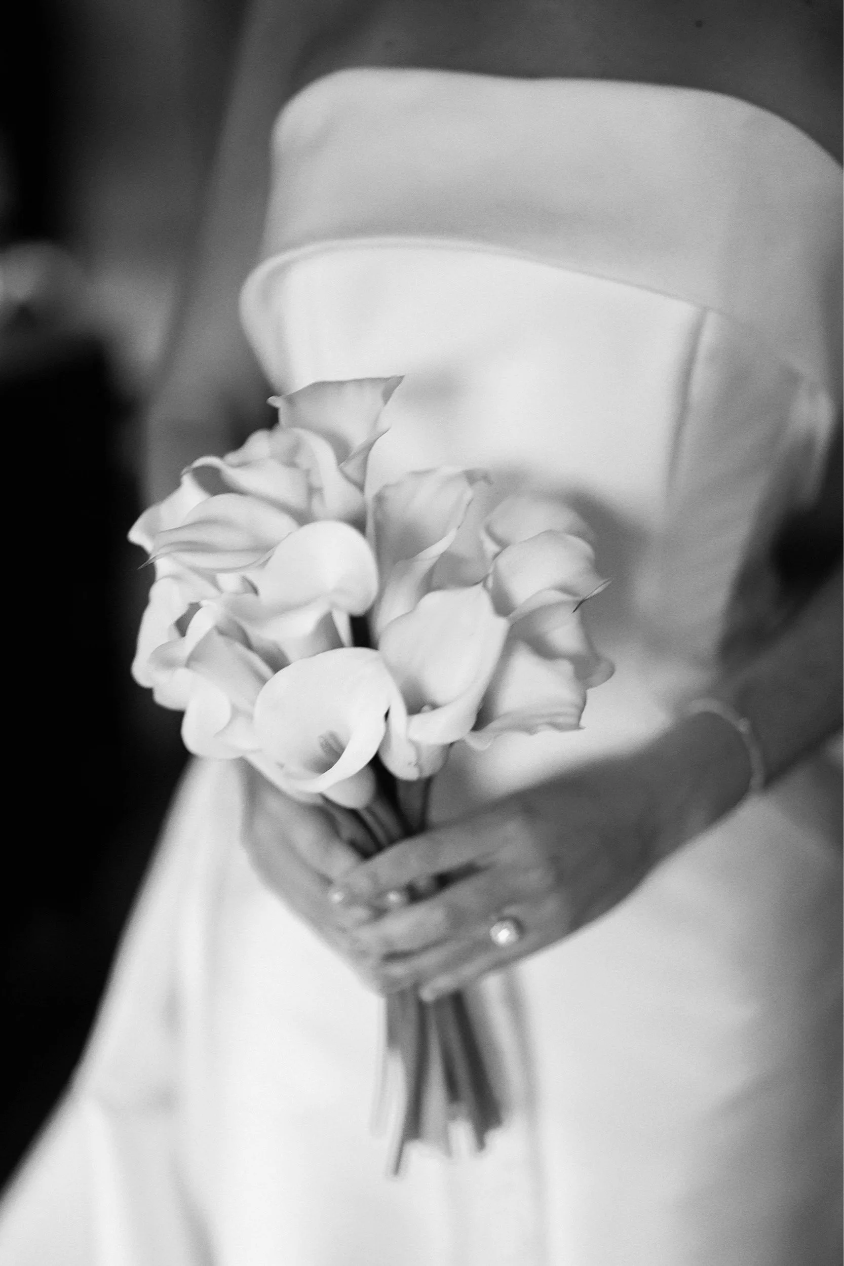 A person in a white dress holding a bouquet of white calla lilies.