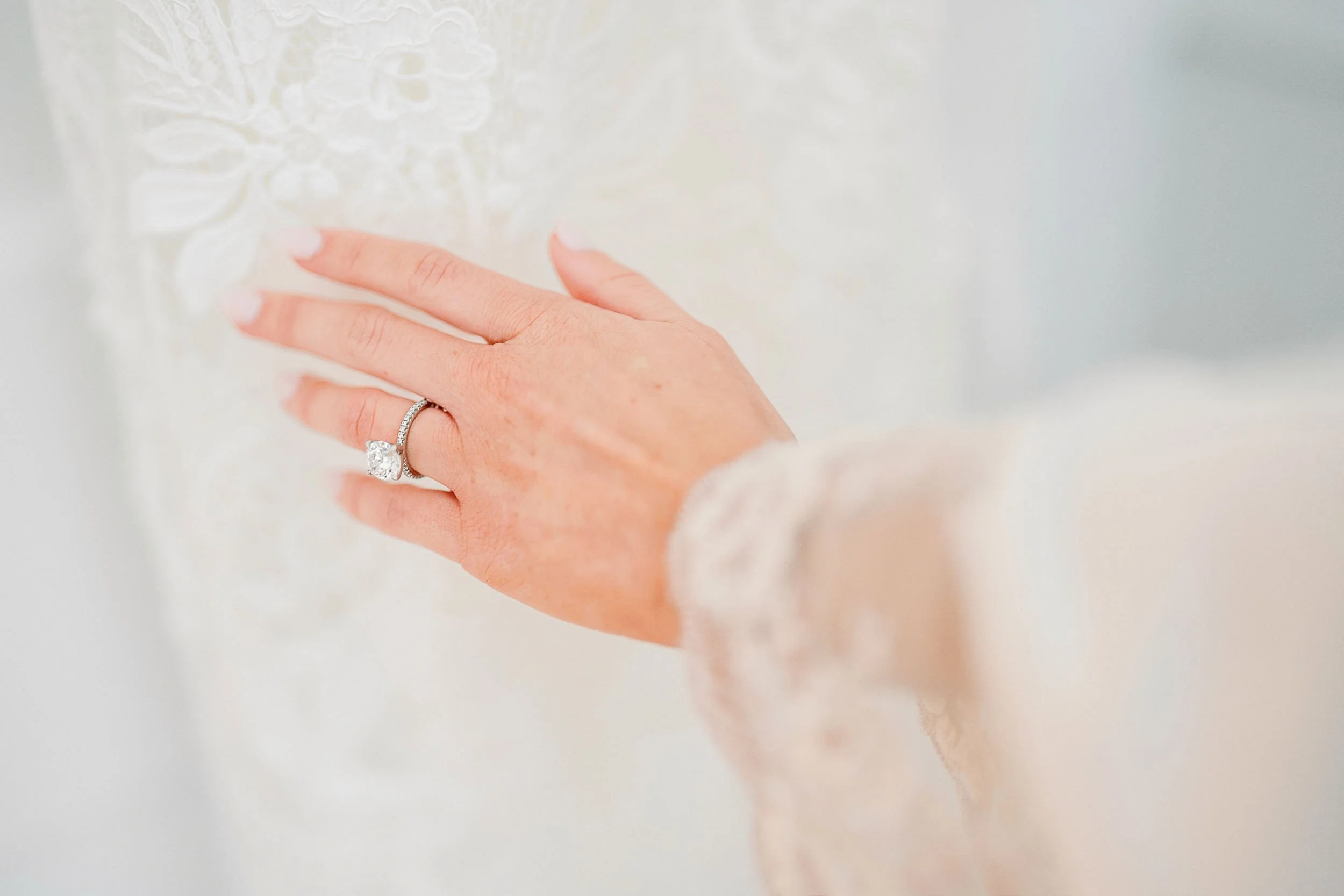 Close-up of a woman's hand wearing a diamond engagement ring, touching a white textured surface.