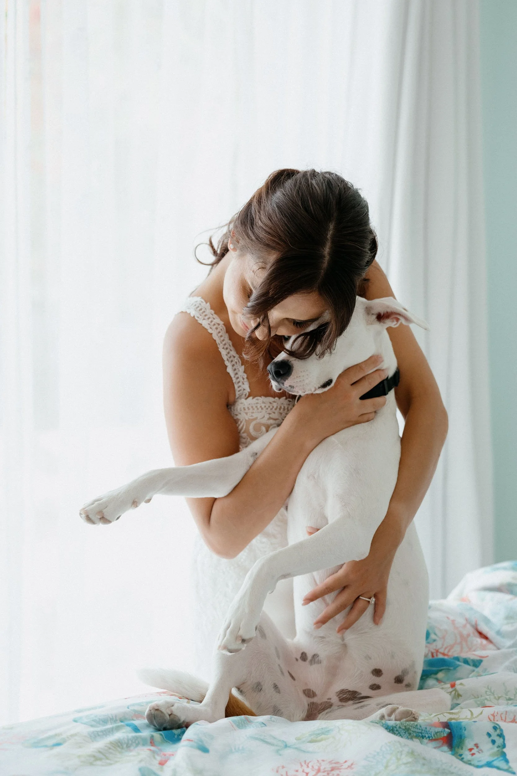 A woman hugging a white dog with brown spots inside a bright room.