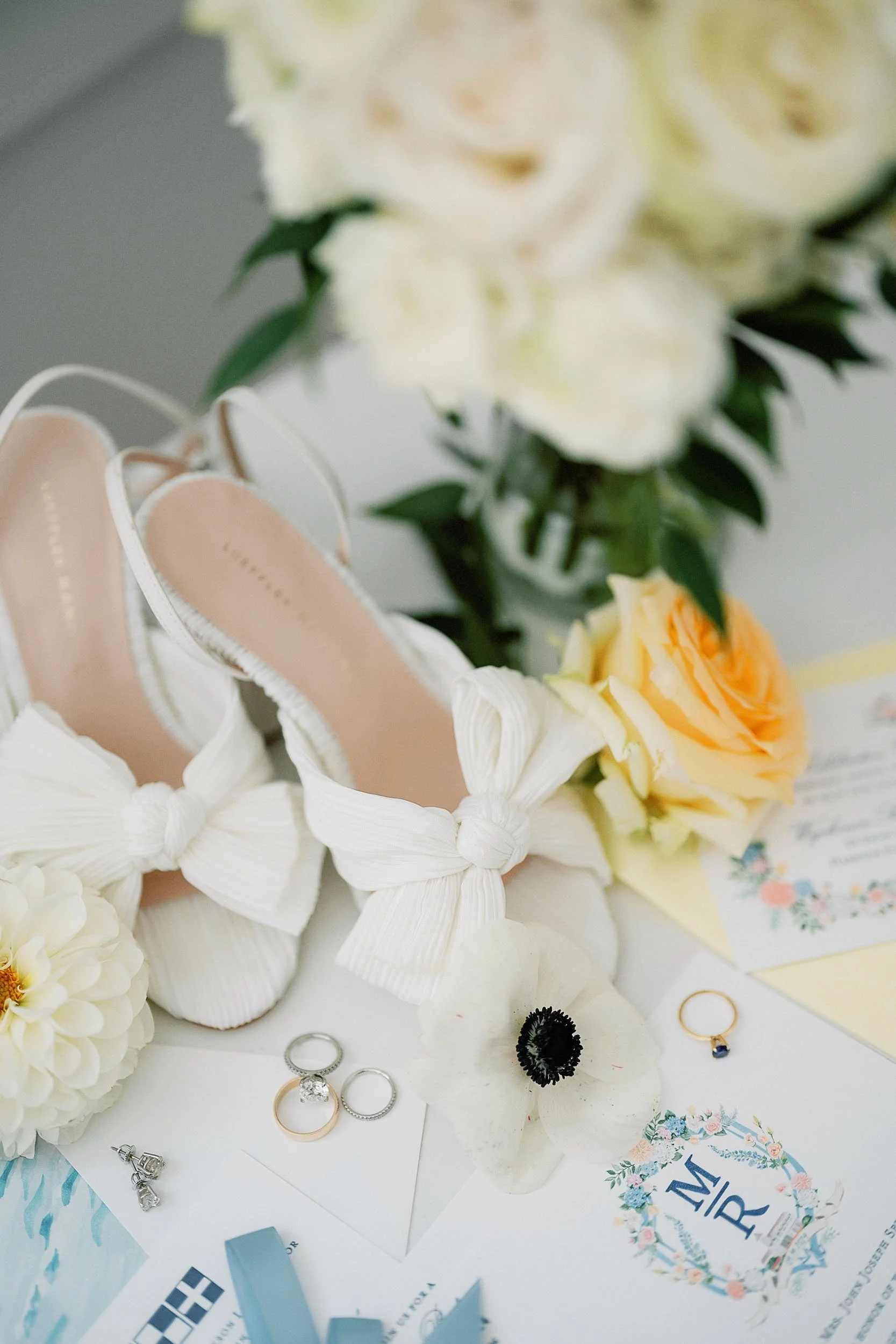 Wedding shoes, bouquet, rings, and invitation on a table.