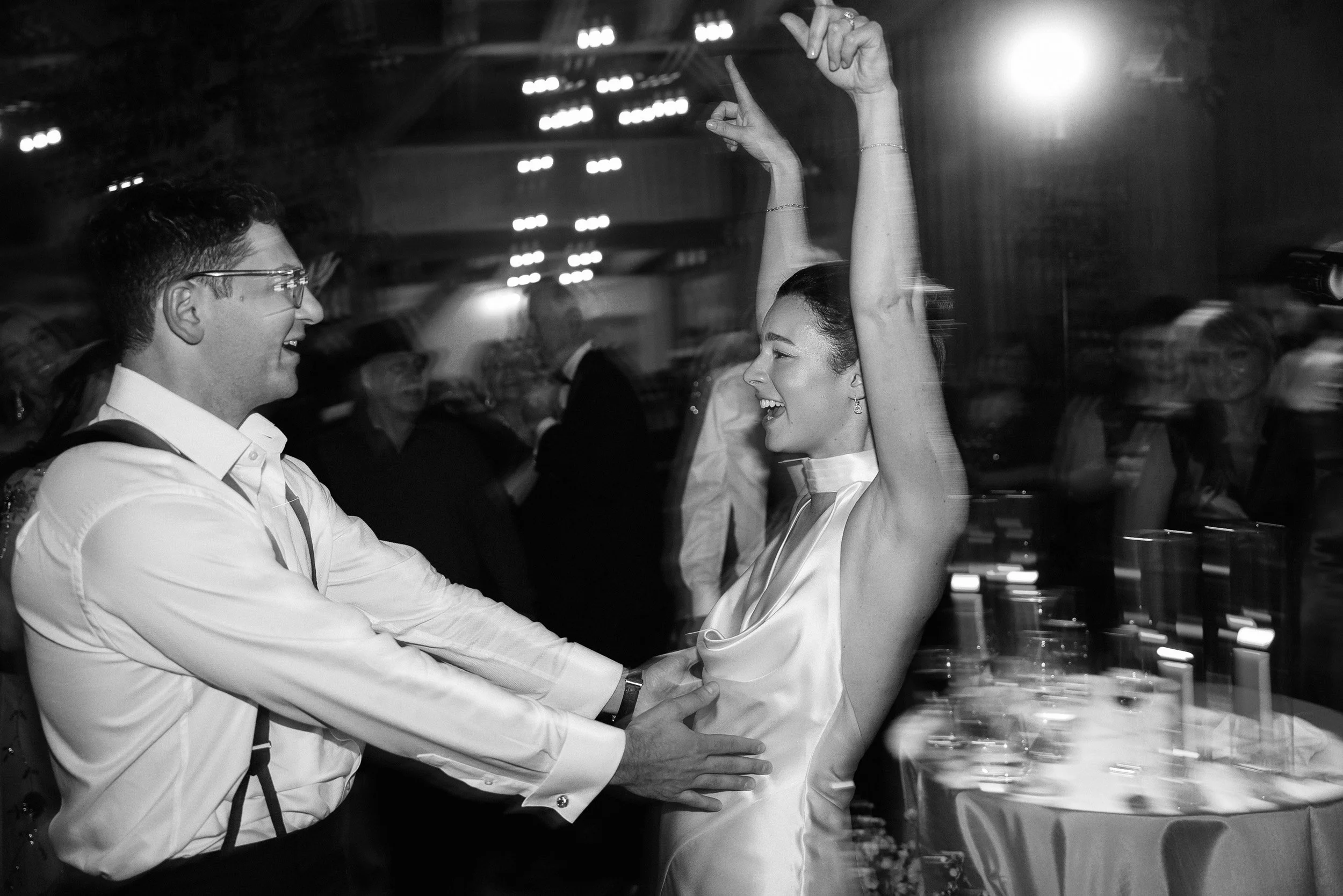 A man and woman dancing at a celebration, with the woman smiling and raising her arms.
