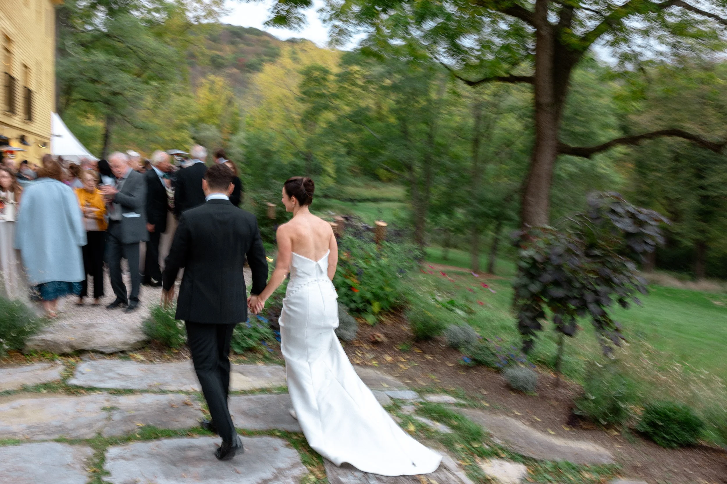 Bride and groom walking hand in hand on a stone pathway during outdoor wedding reception