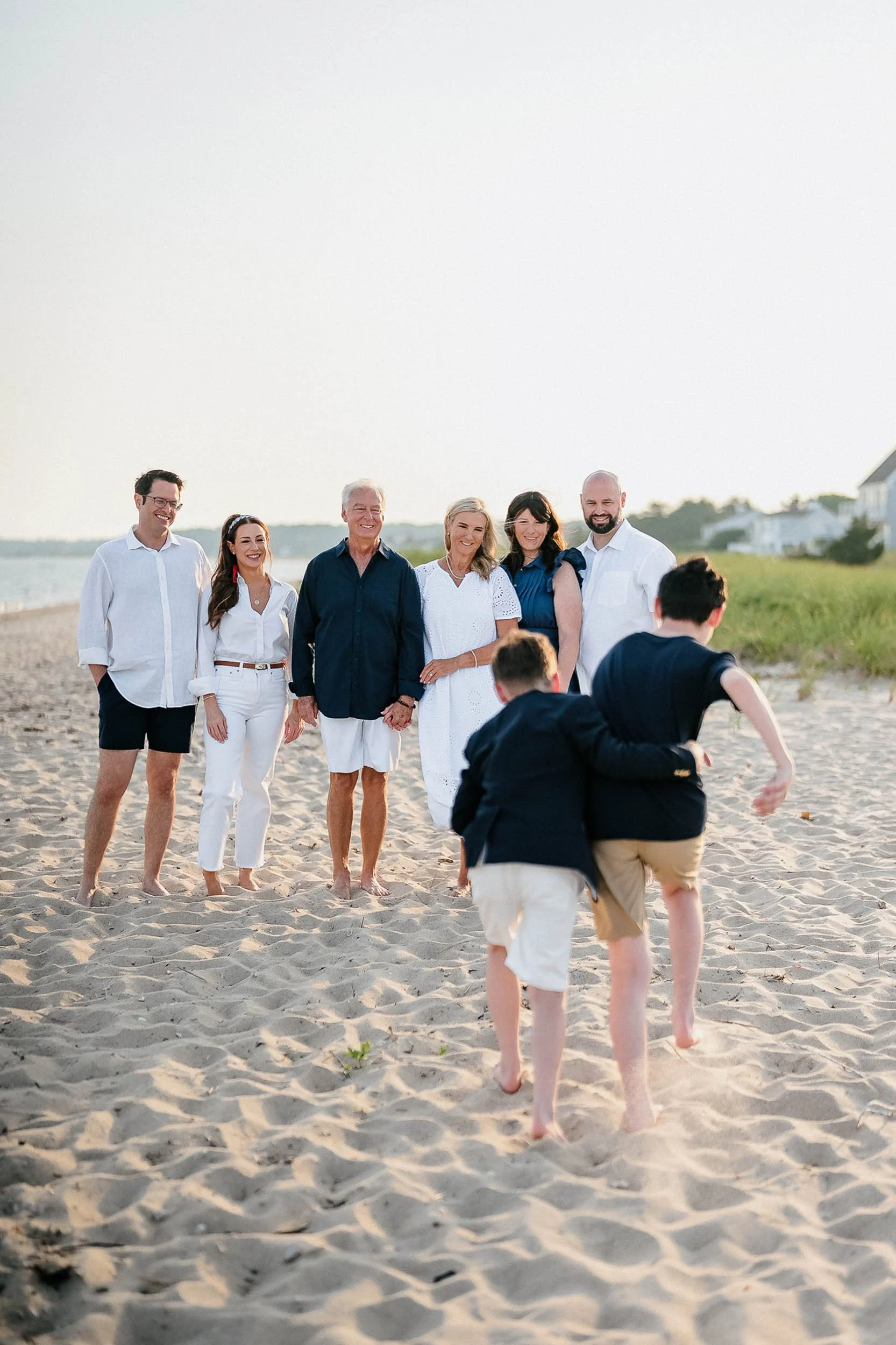 Family at the beach, with seven adults standing together in a line and two children running towards them.