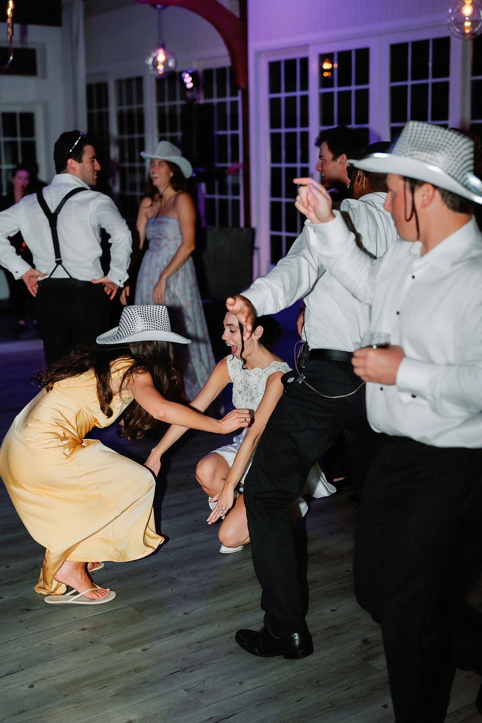 People dancing and enjoying themselves at a lively event or party, with some wearing cowboy hats and formal attire.