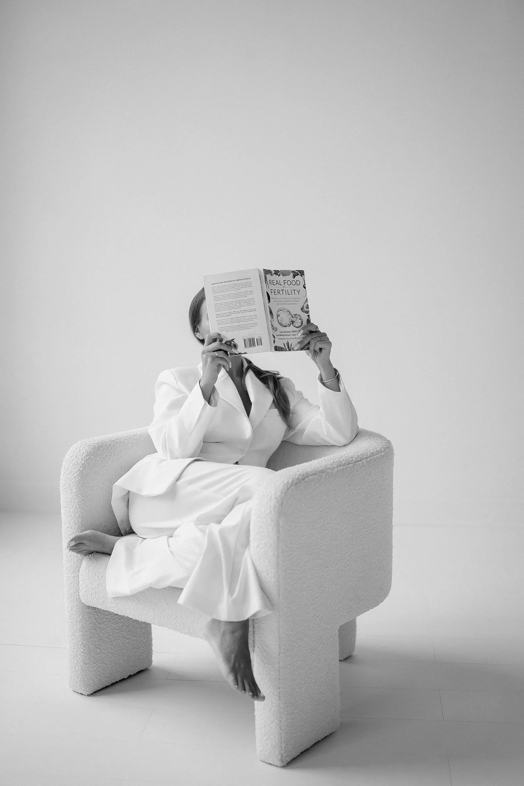 Personal branding photoshoot near Boston with woman in white suit sitting and reading in minimalist studio