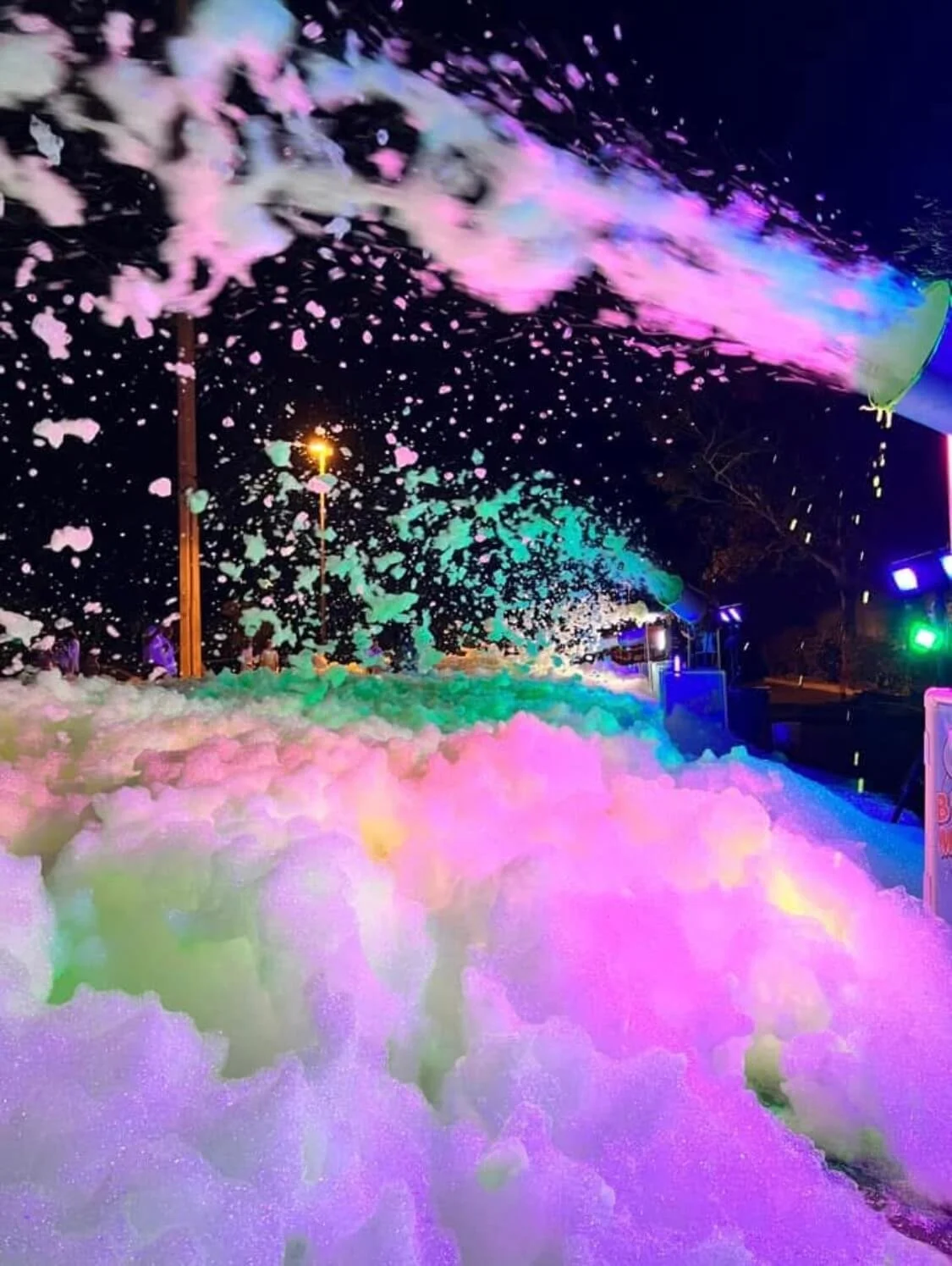 Colorful foam dance floor lit up in green and pink at night with foam cannons in action