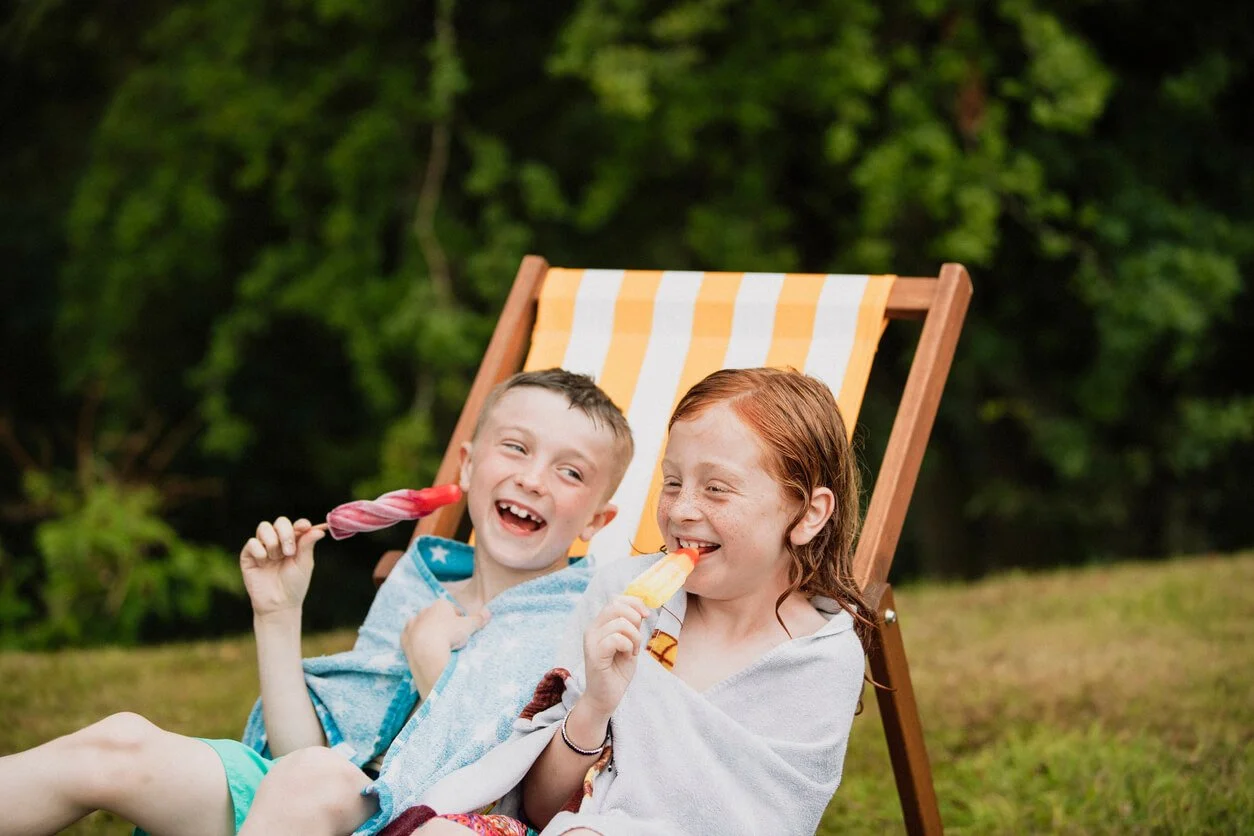 Two kids wrapped in towels, laughing and enjoying popsicles after a foam party