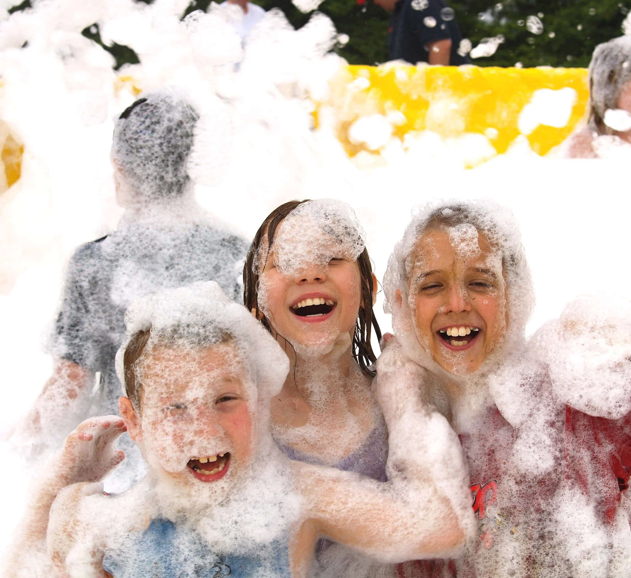 Three kids covered in foam at a retro block party foam event, celebrating classic summer fun with laughter and friends