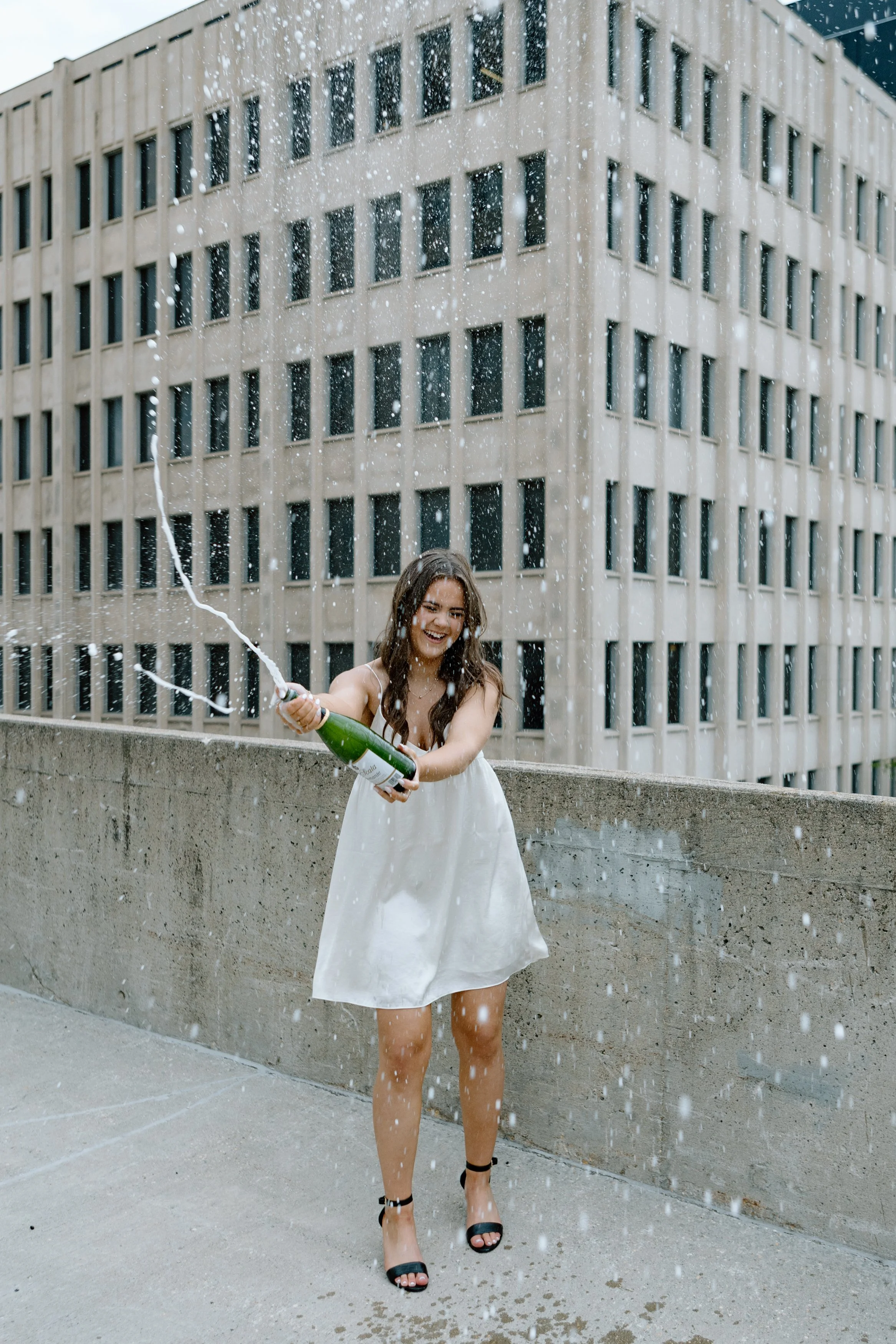 Graduation session with a champagne pop on a rooftop in downtown Winnipeg, featuring a luxury vibe with the graduate in an Aritzia dress, capturing a high-end celebration.