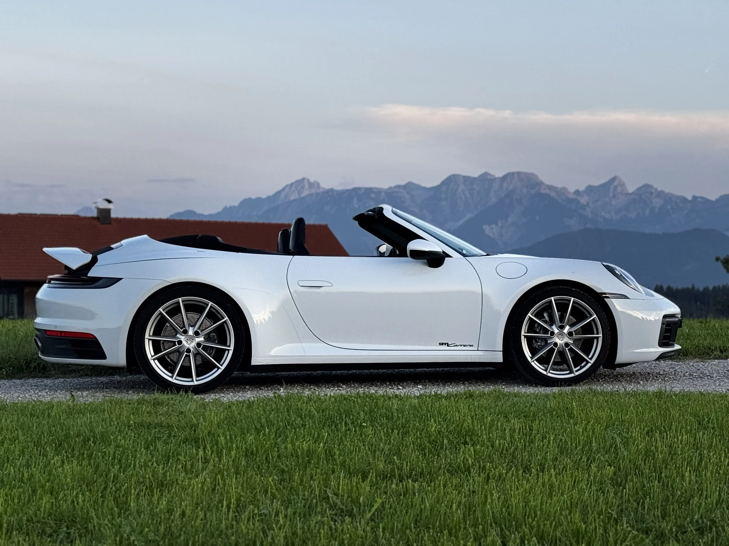Weißer Porsche 911 Cabrio auf einer Wiese mit Bergen im Hintergrund