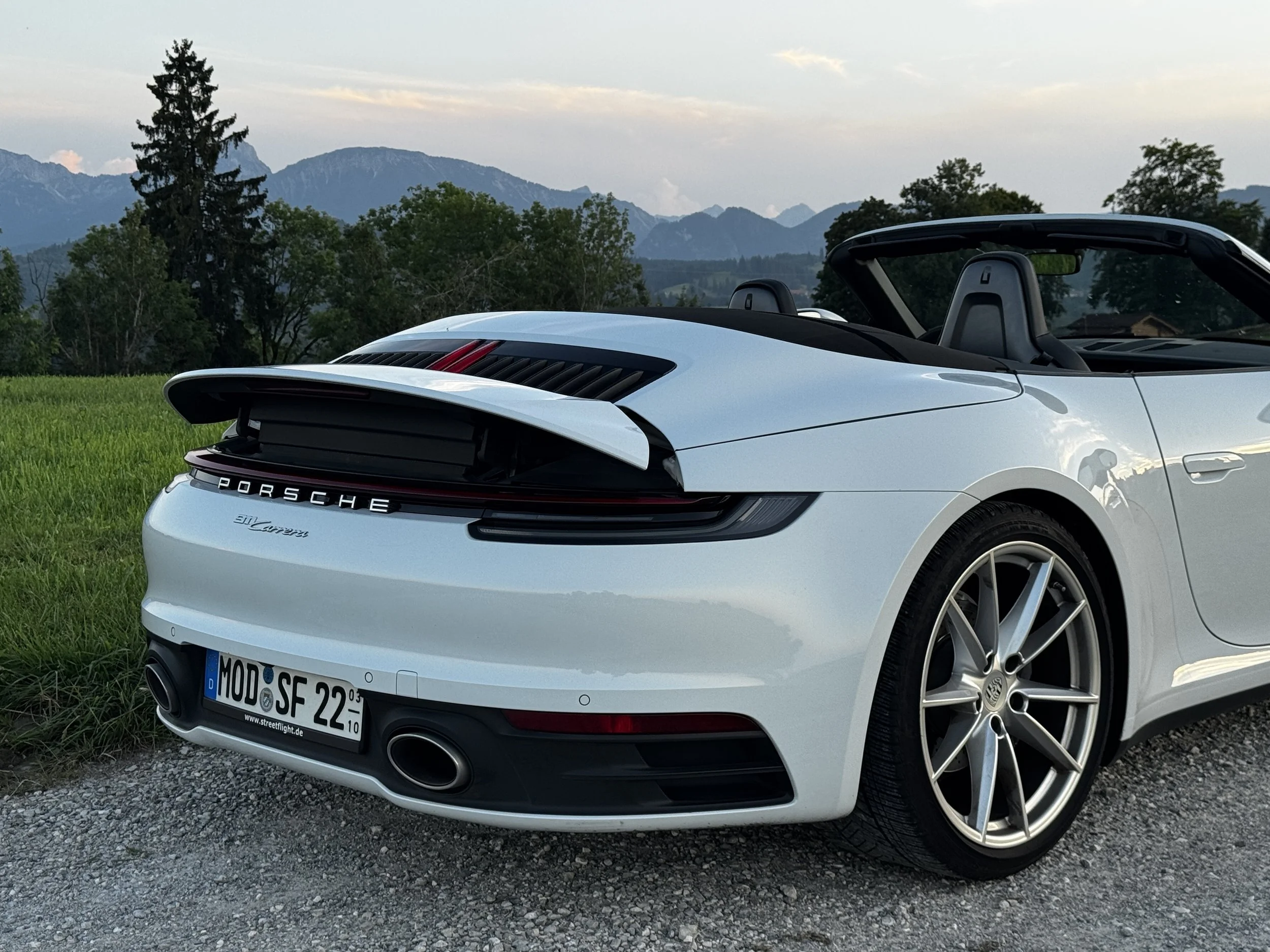 Weiße Porsche 911 Cabriolet auf einem Feld mit Bergen im Hintergrund