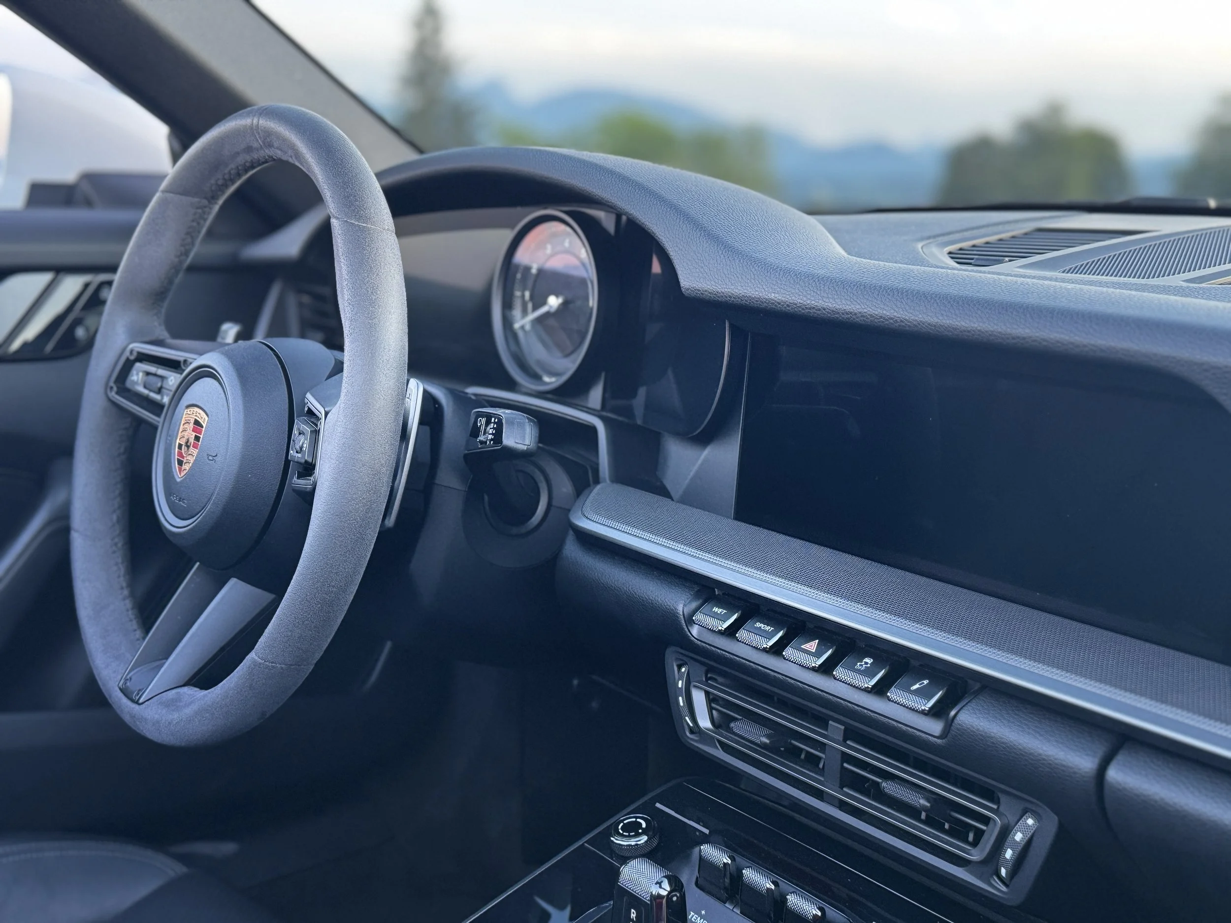 Innenansicht eines Porsche-Fahrzeugs mit Lenkrad, Armaturenbrett und Bedienelementen.