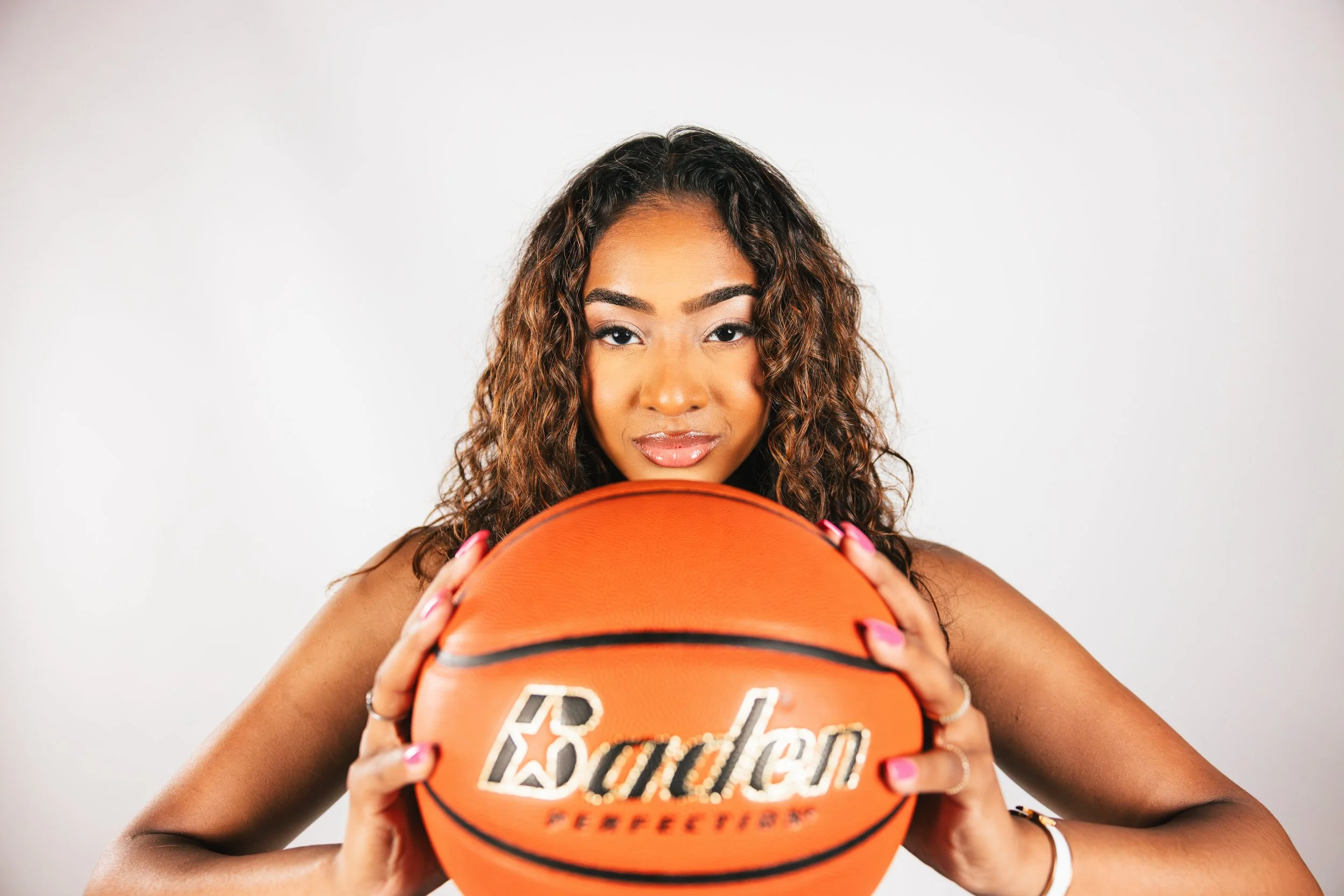 A woman with curly hair holding a basketball facing the camera.