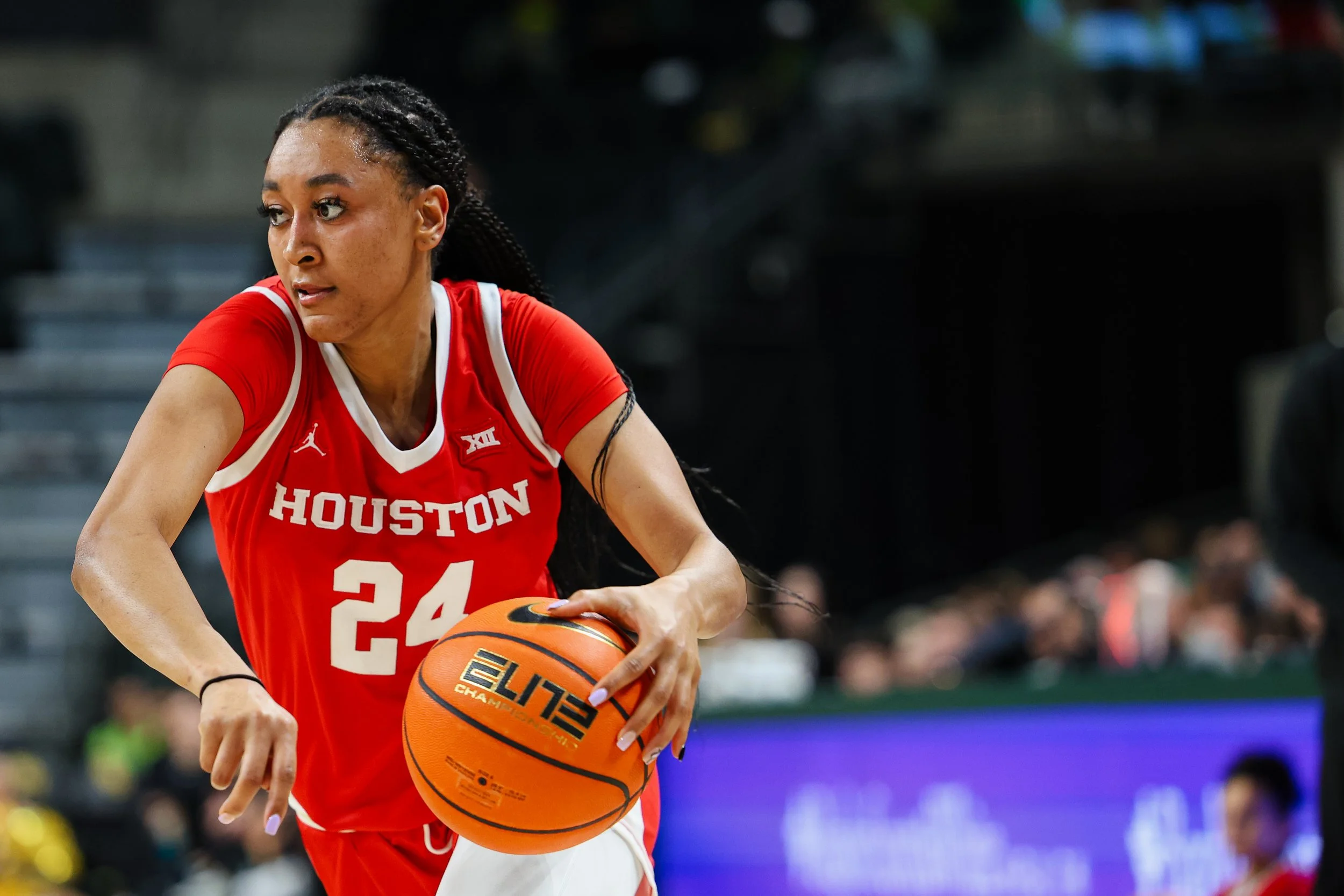 A female basketball player wearing a red Houston jersey with the number 24 dribbling a basketball on the court.