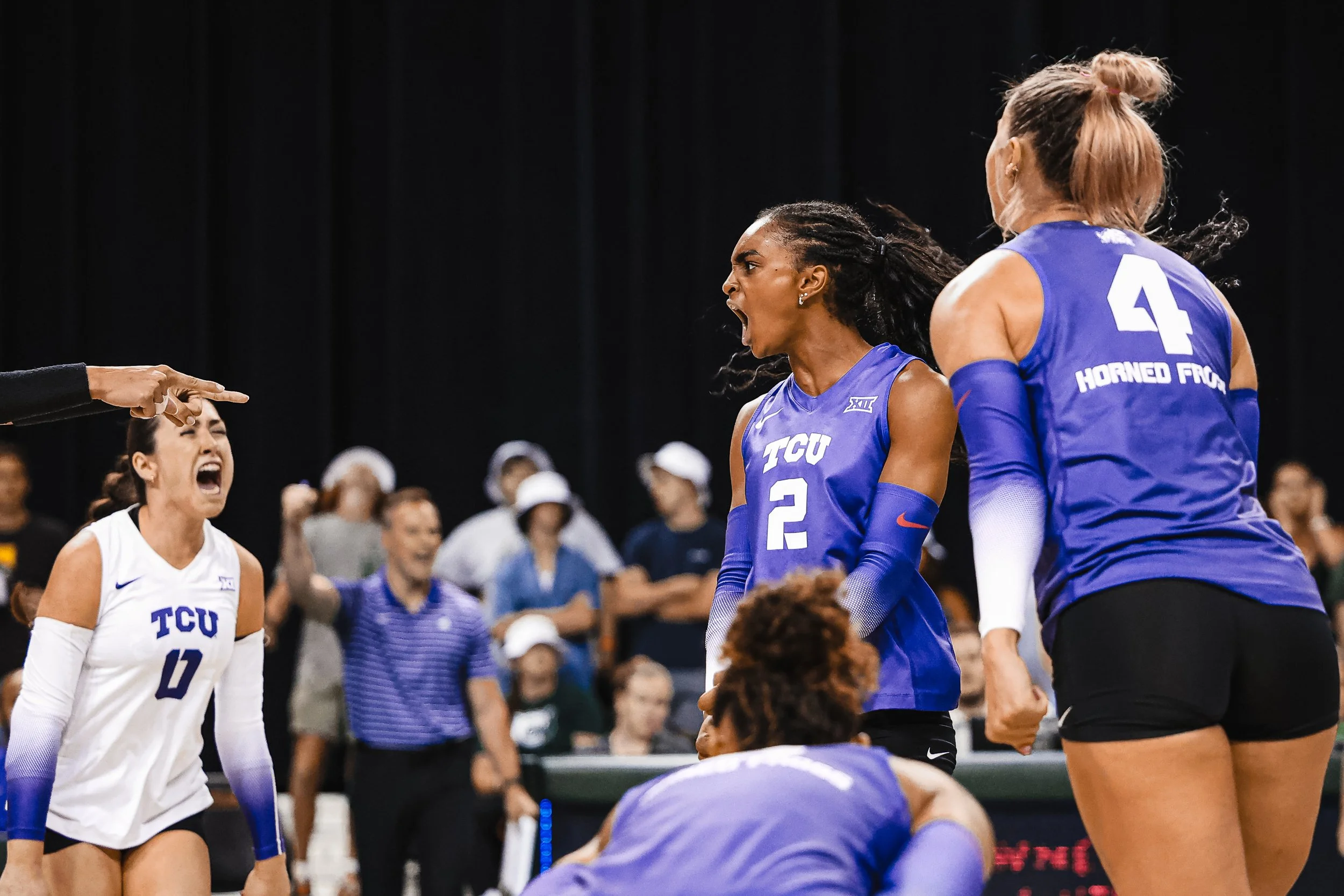 Women's volleyball team from TCU celebrating on the court during a game, with players wearing blue and white jerseys.
