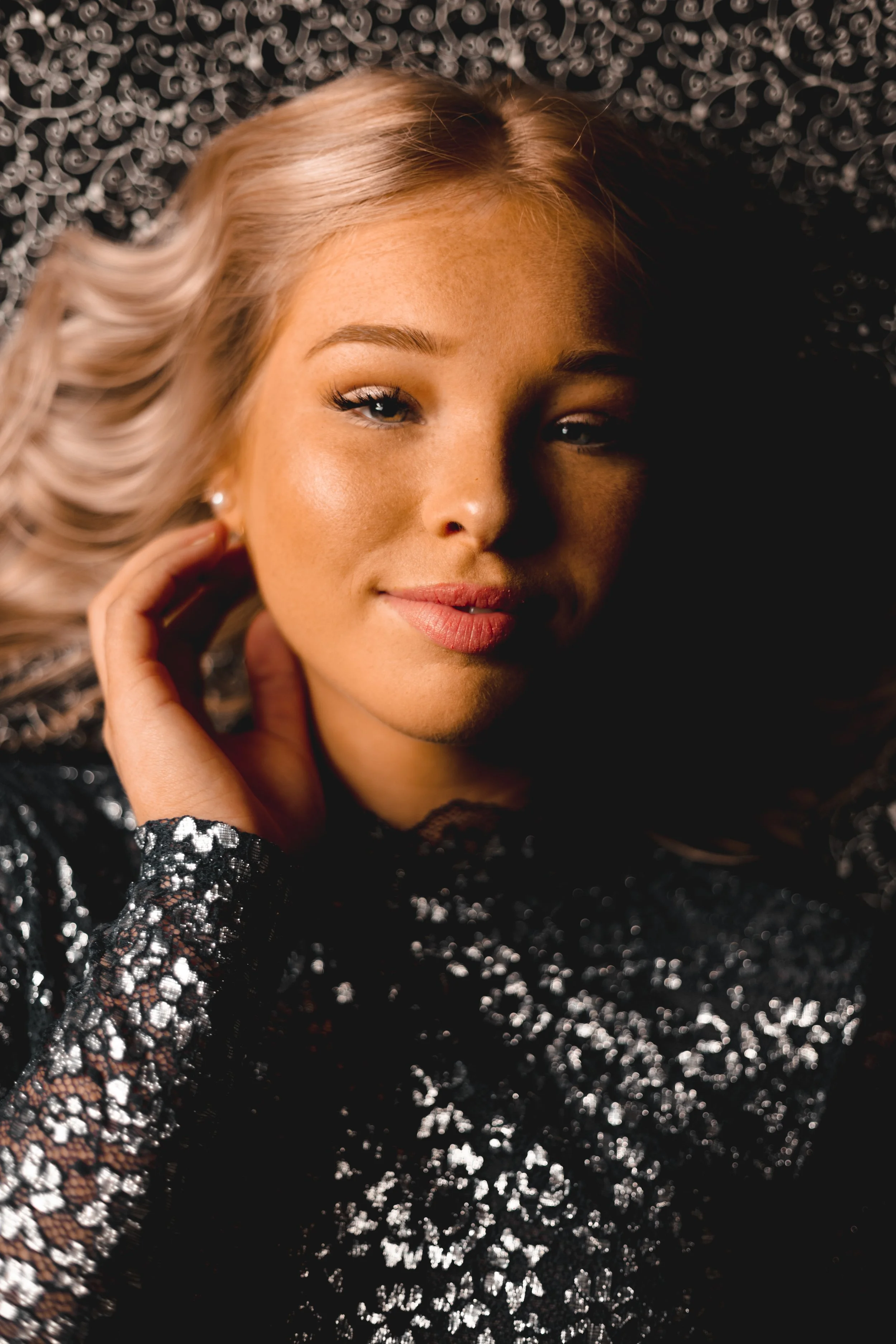 A woman with blonde hair and fair skin lying down on a black and silver sequin dress.