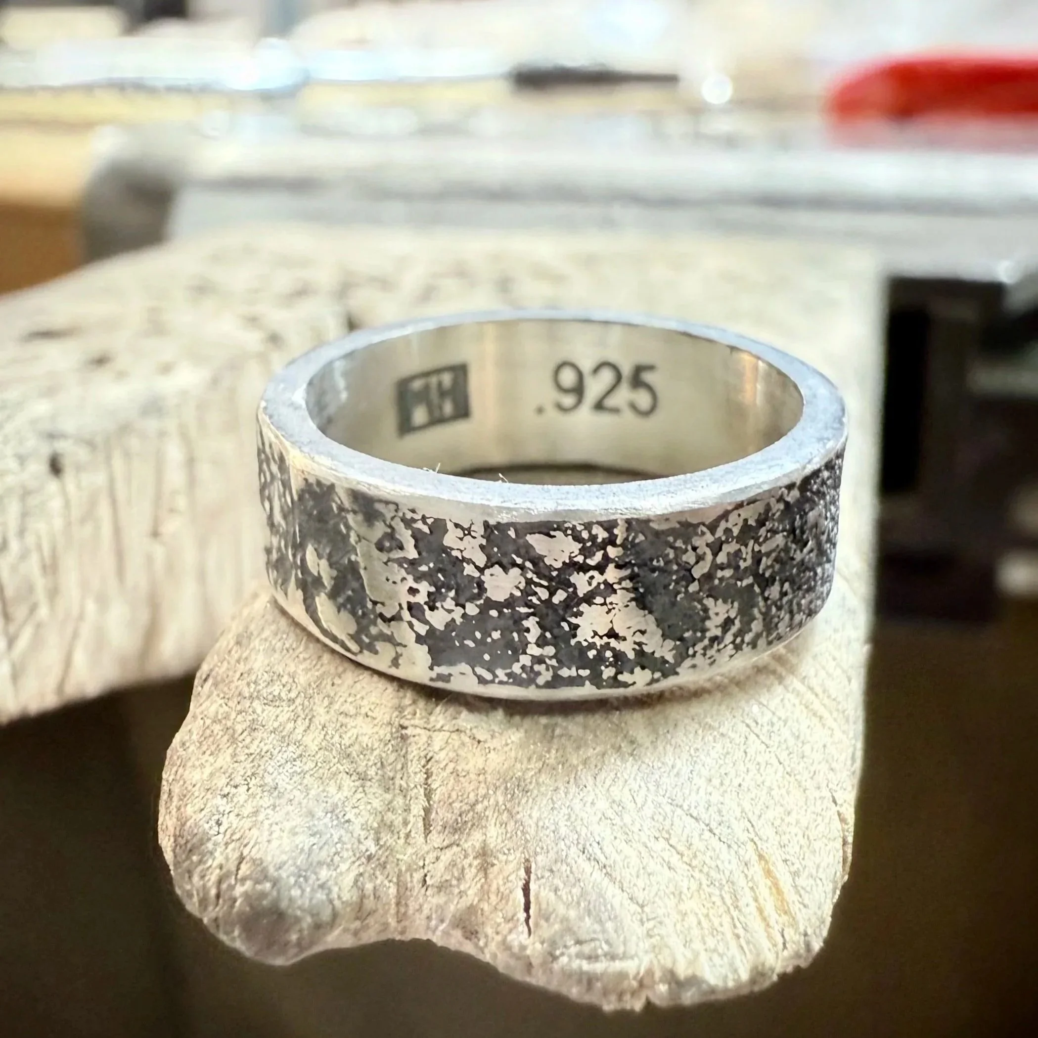 A silver ring with a textured, speckled black and silver pattern, engraved inside with '925' indicating sterling silver, and an MLH Designs hallmark logo.