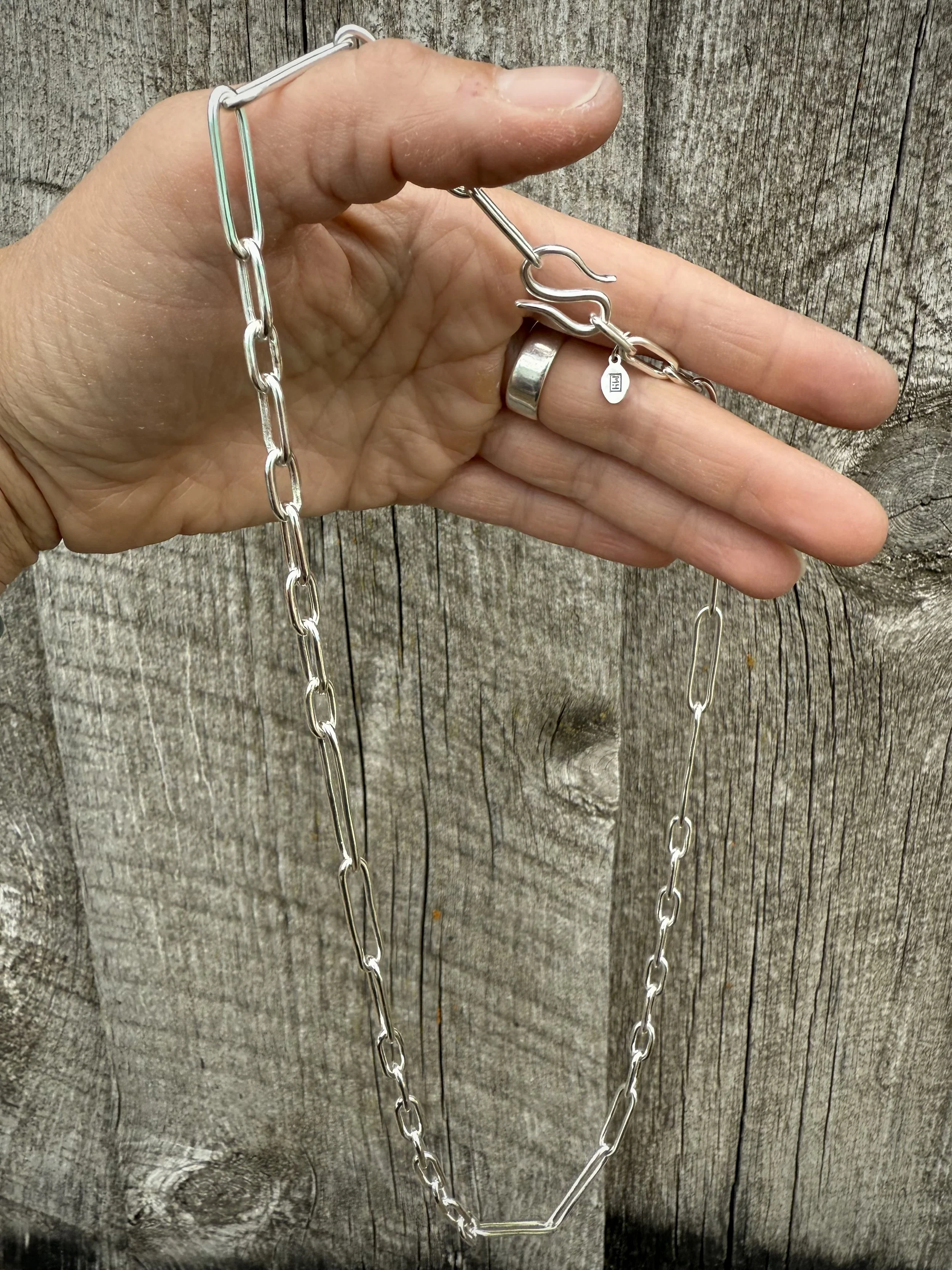 Hand holding a silver chain necklace with a clasp, set against a wooden background.