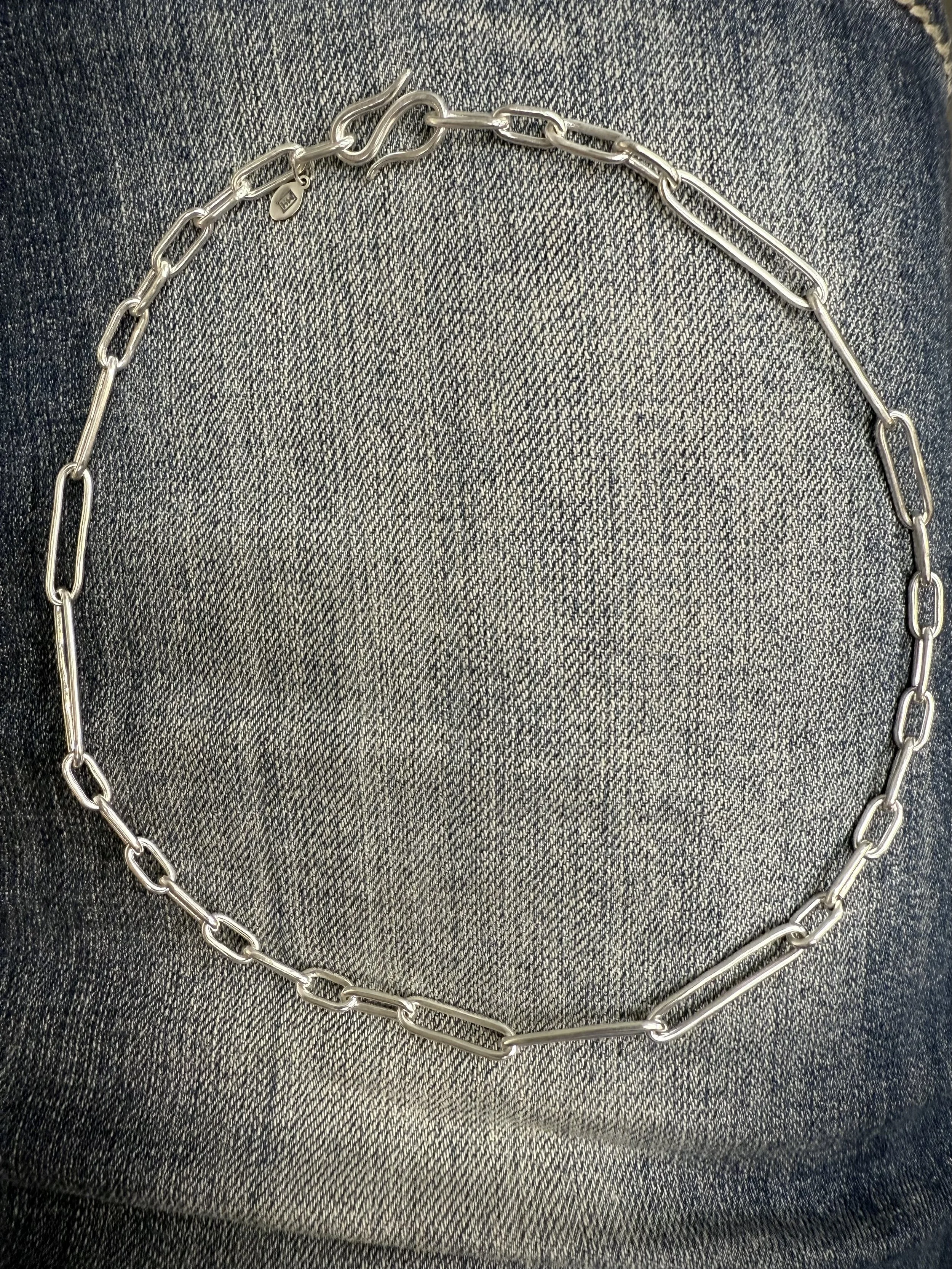 Silver chain necklace with large and small links resting on denim fabric.