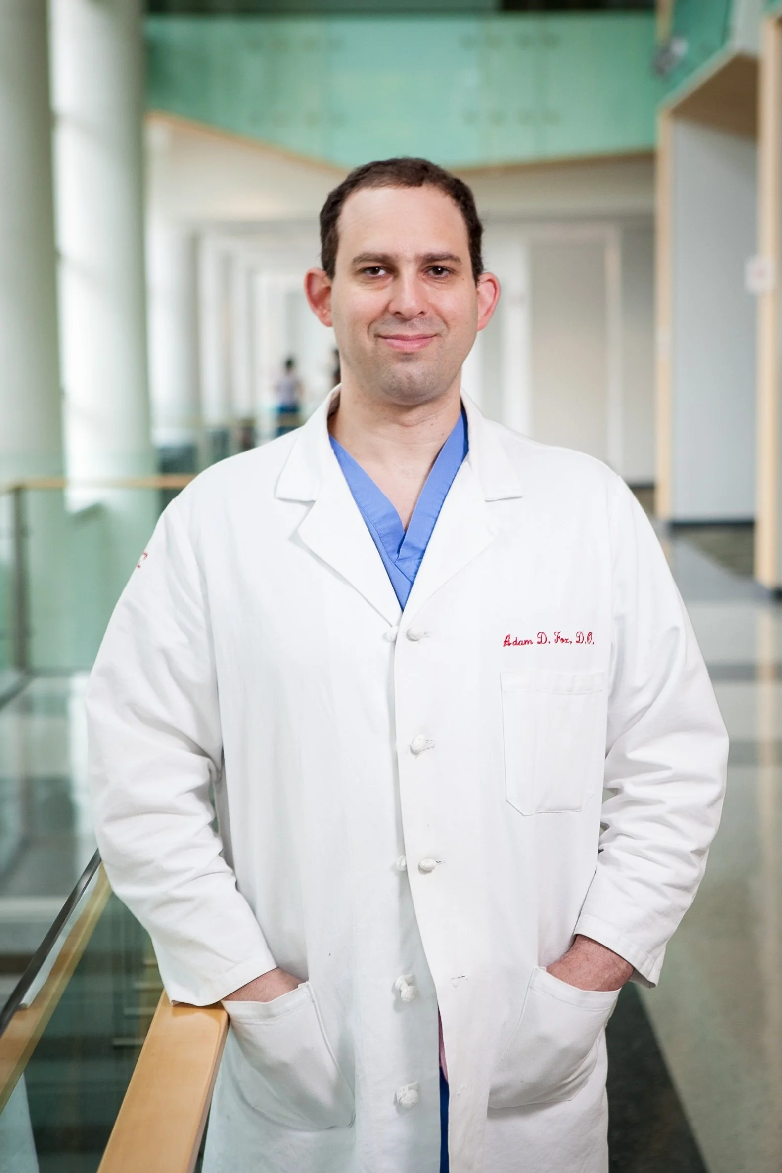 A male doctor in a white coat standing in a hospital corridor.