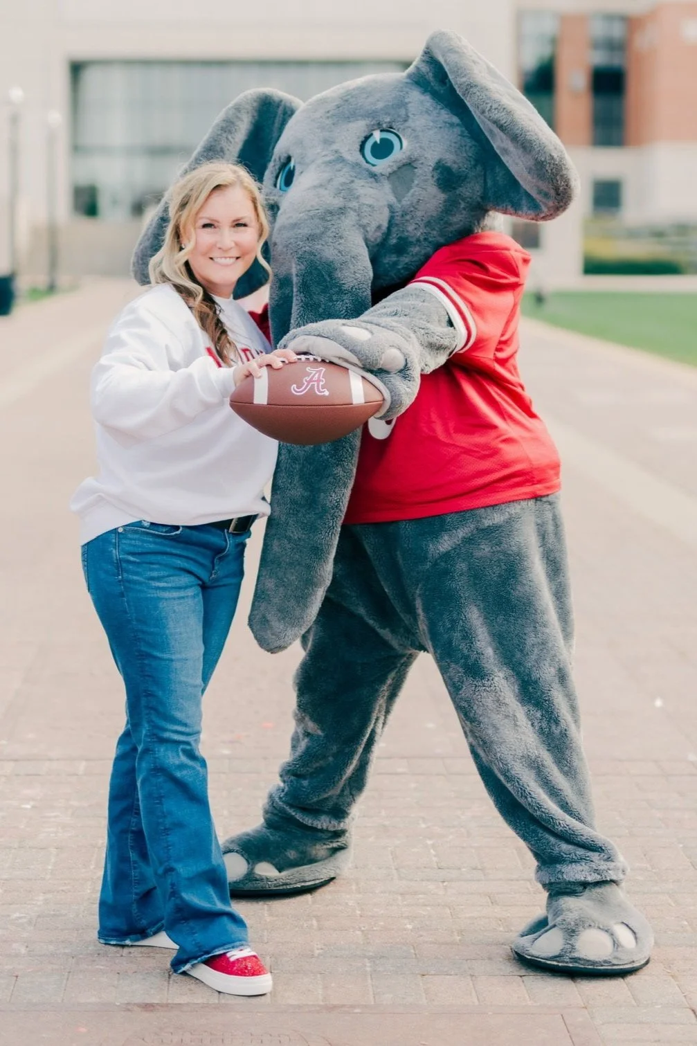 A woman and a person in an elephant mascot costume holding an Alabama football.