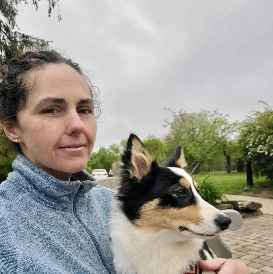 Woman sitting outdoors with a black, white, and tan Australian Shepherd puppy.