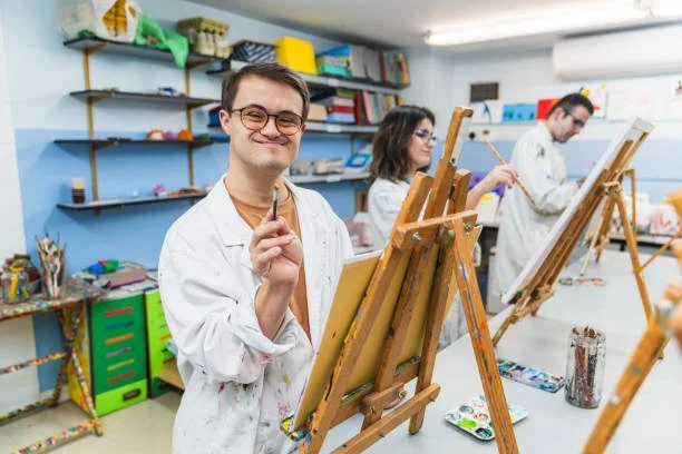 Group of young adults painting on canvases set up on easels in an art studio.