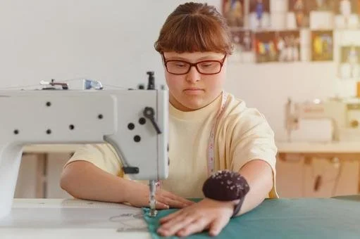 Young woman with red glasses sewing a black cupcake onto fabric in a sewing workshop.