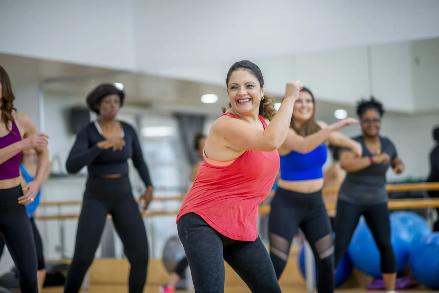 Women participating in a dance fitness class in a gym, smiling and moving energetically.