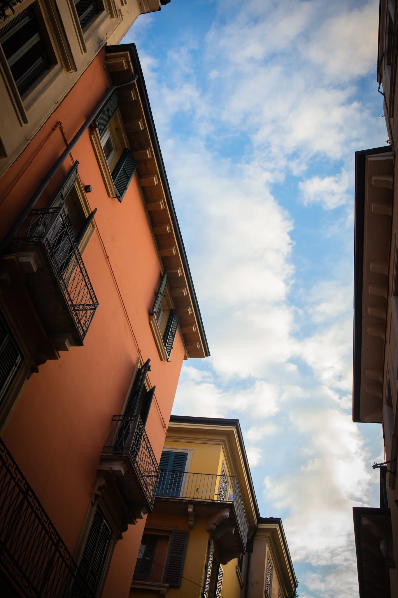 View of colorful buildings with balconies and a cloudy blue sky overhead.