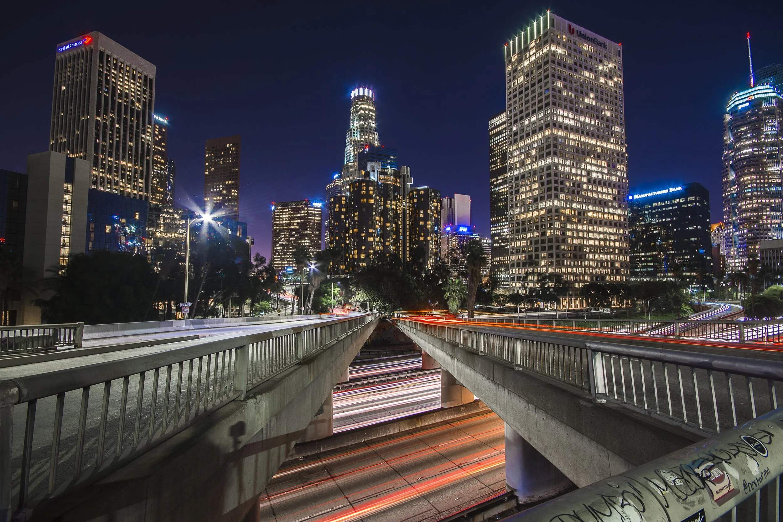 Downtown Los Angeles cityscape at night with skyscrapers and light trails from traffic.