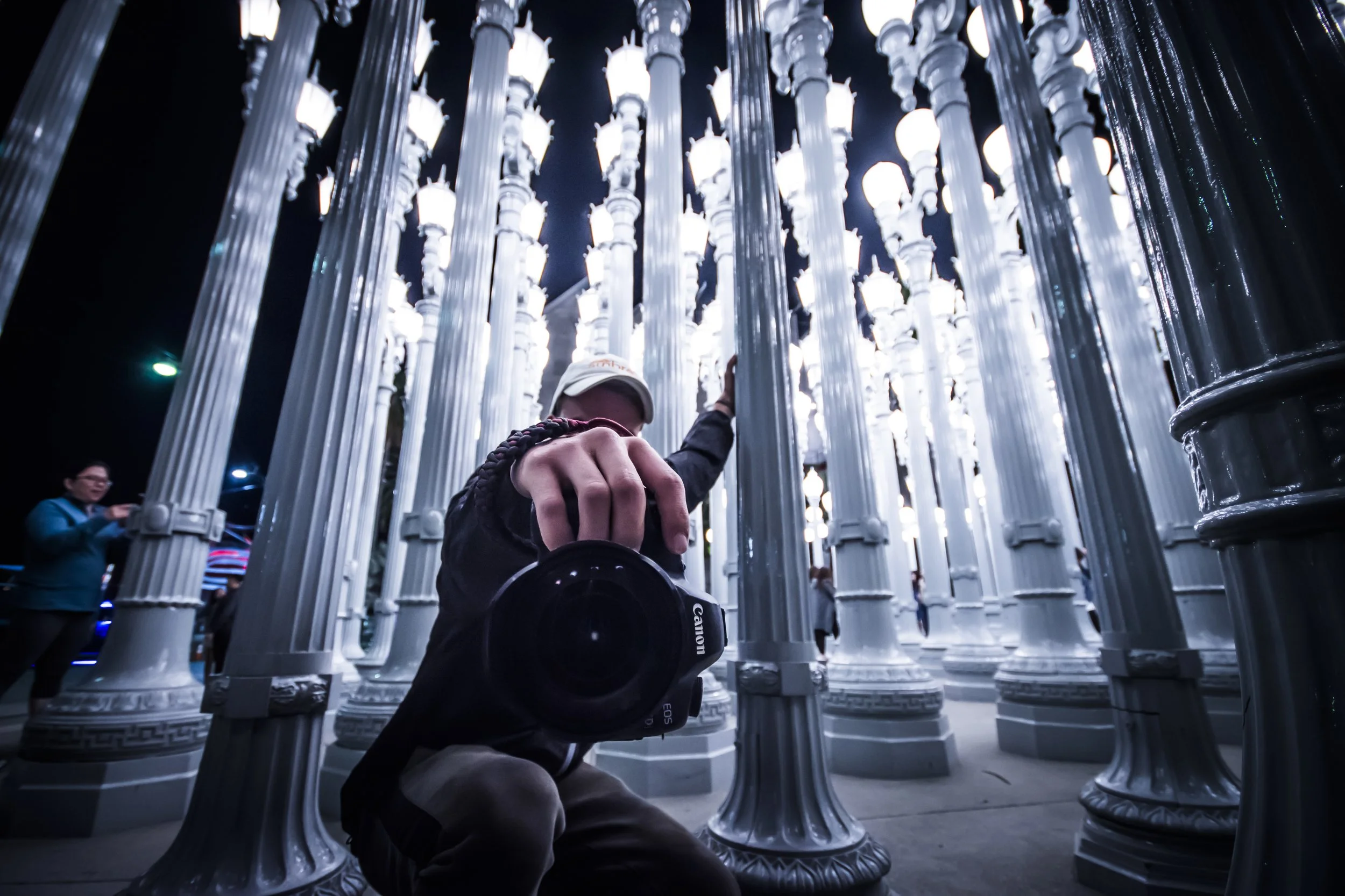 Person holding camera near illuminated streetlight installation at night.