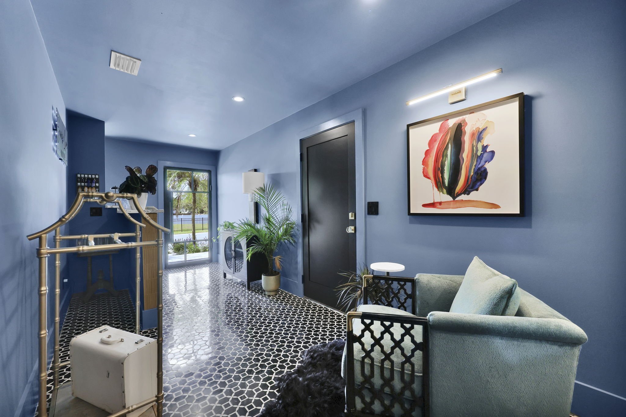 Interior of a modern blue room with black door, abstract art on the wall, stylish armchair, plants, and geometric floor tiles.