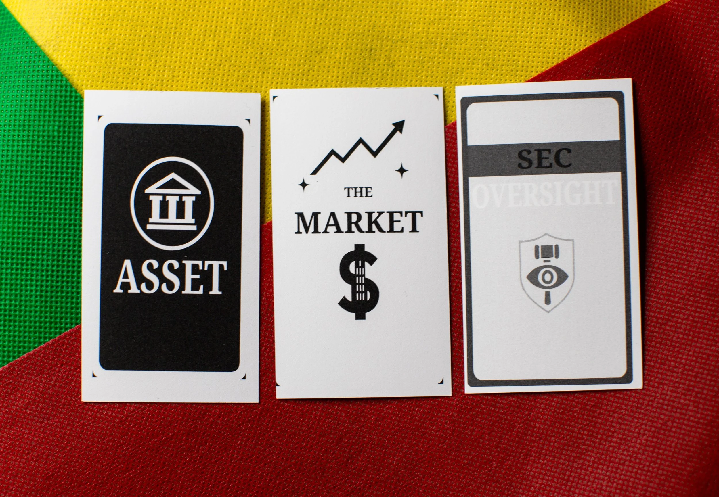 Three cards with financial and regulatory terminology, from left to right: Asset, The Market, SEC Oversight, placed on a multicolored fabric background.