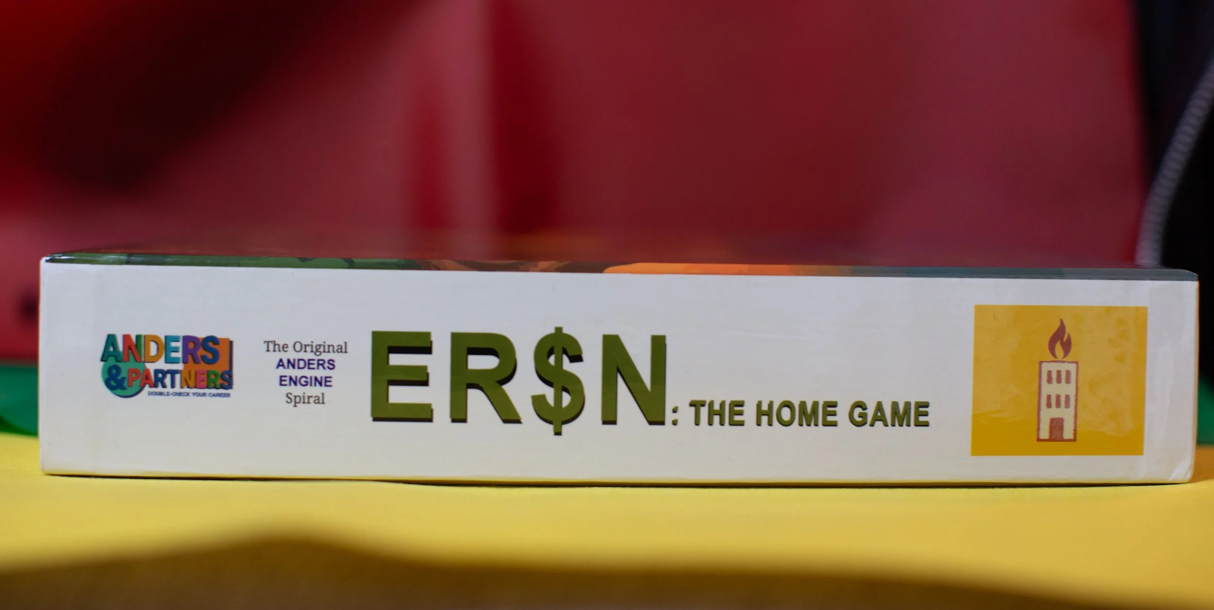 The box of a game called 'ERSN: The Home Game'. It is an Anderson & Partners product, with colorful text and a yellow logo on the right showing a burning candle or flame on a tall structure.