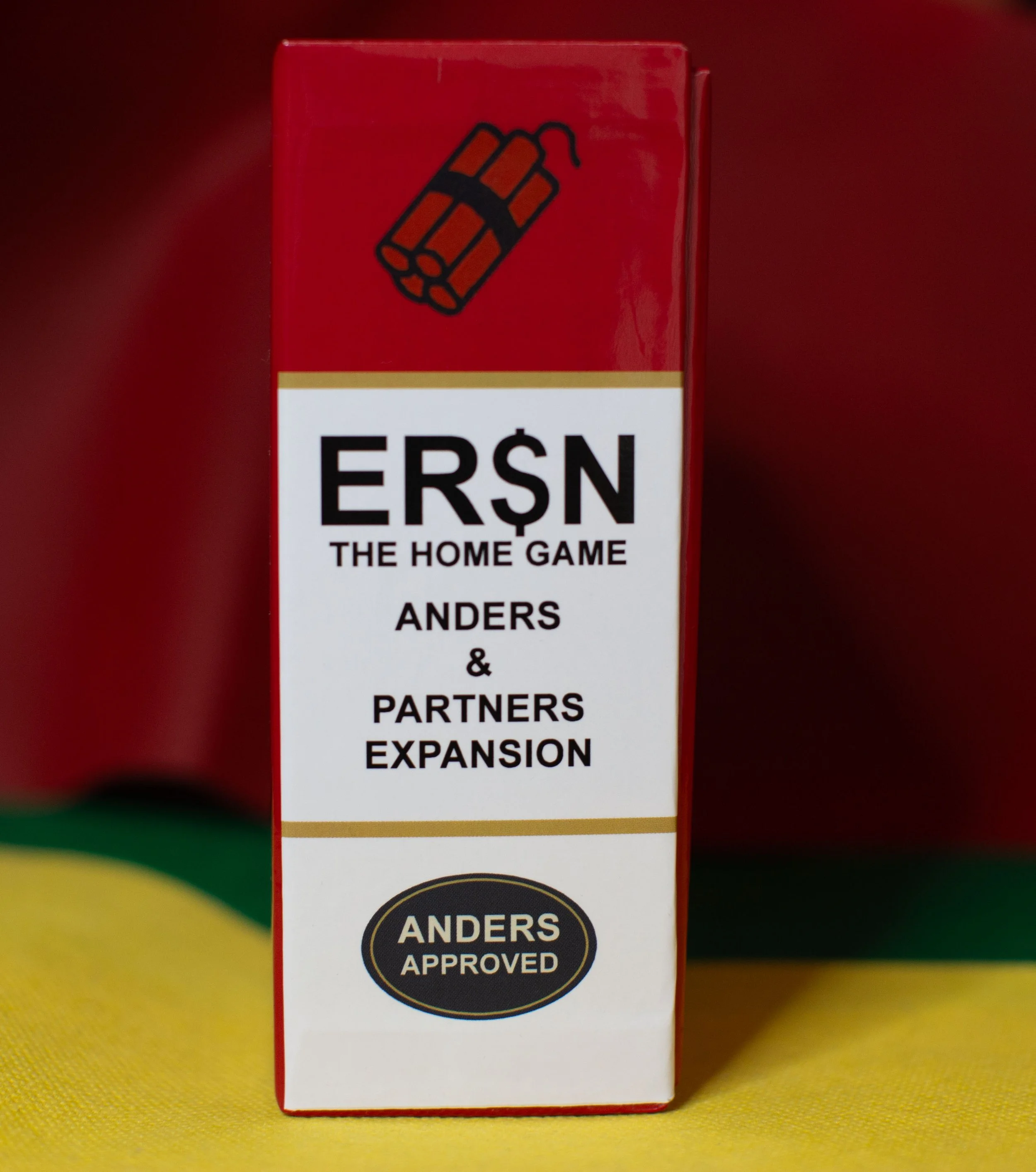 A red box with the title "ERŞN: The Home Game" and the subtitle "Anders & Partners Expansion" with an icon of dynamite on top and an