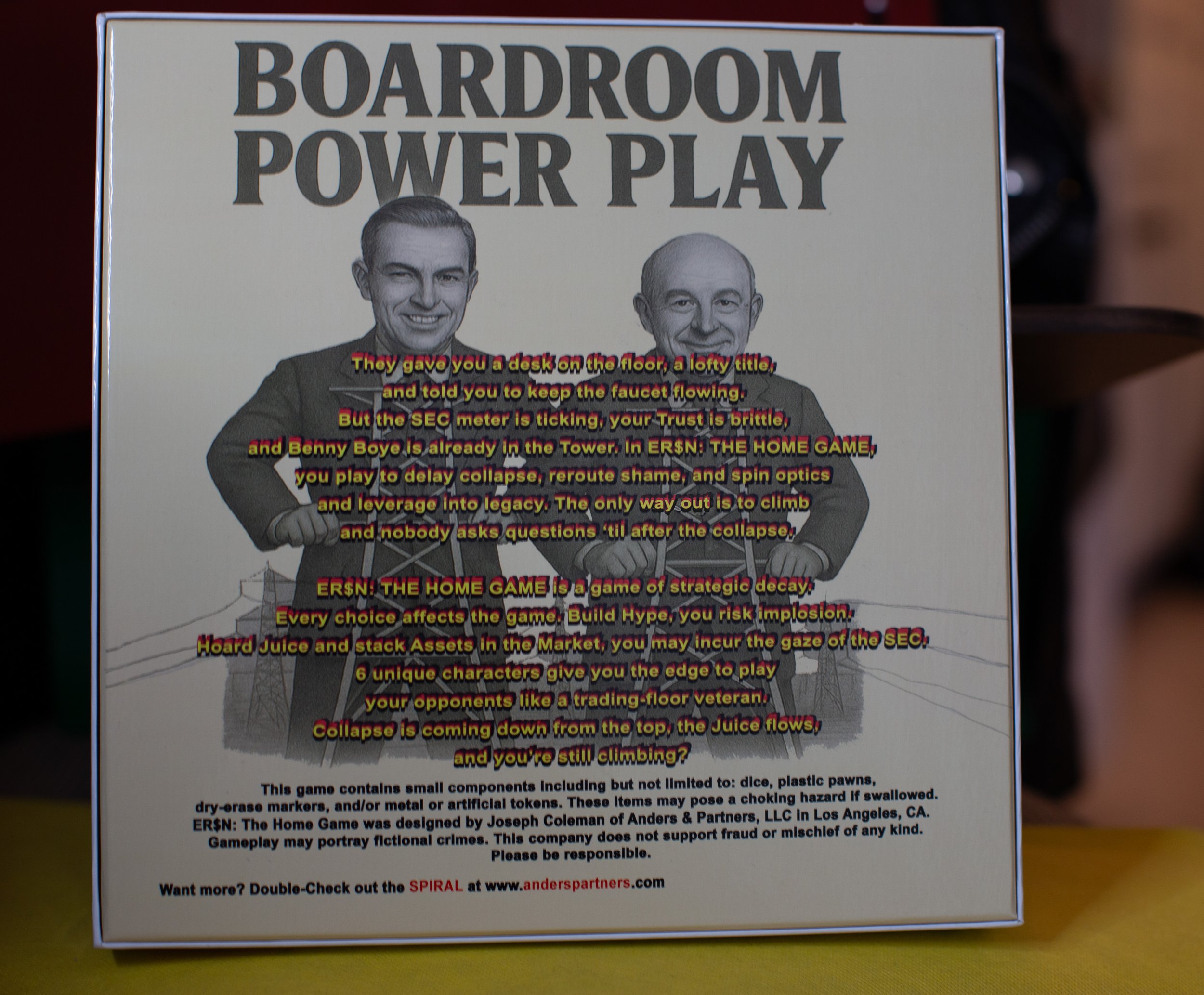 A game box titled "Boardroom Power Play" with caricatures of two men in suits holding batons, standing in front of a bridge. The box has humorous and satirical text about strategic decay, market manipulation, and game tactics.