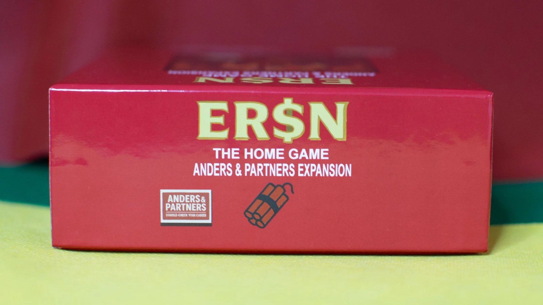 Red box for the game Erşn: The Home Game Anders & Partners Expansion with a small graphic of dynamite on the front.