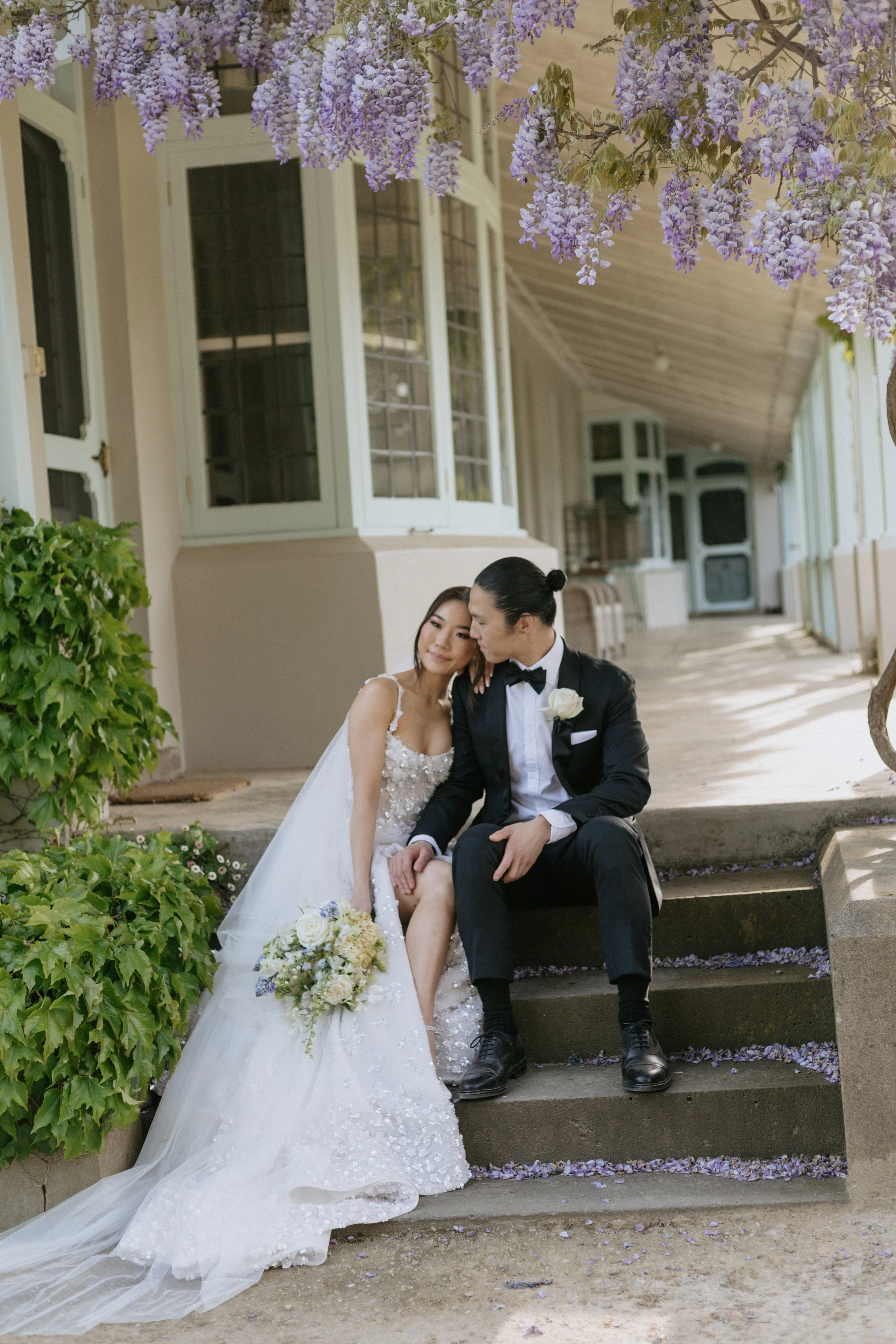 Bride and groom sitting beneath flowering wisteria during their romantic wedding portraits. Coombe Yarra Valley