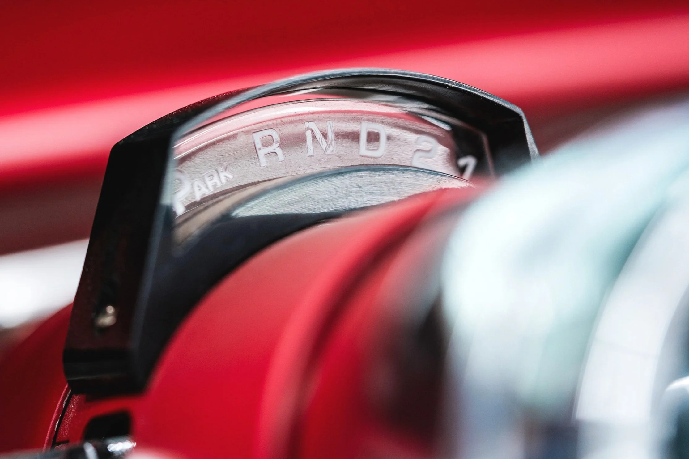 Close-up of a vintage car gear shift lever with a clear view of the gear pattern etched into the metal, showing 'PARK, R, N, D, 2'.