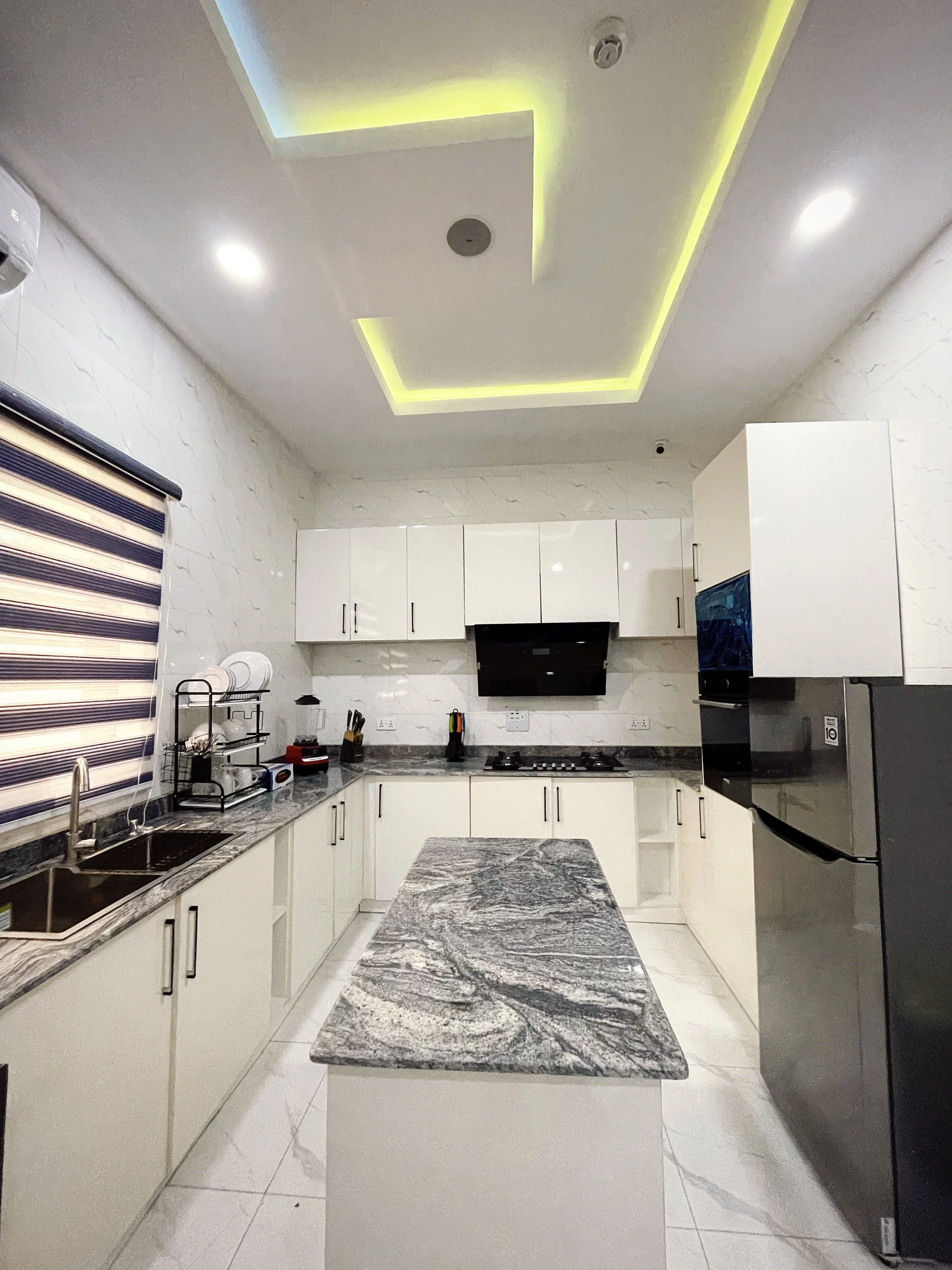Modern kitchen with white cabinets, a gray granite island, stainless steel appliances, and industrial light fixtures. The ceiling features recessed lighting with LED accents.